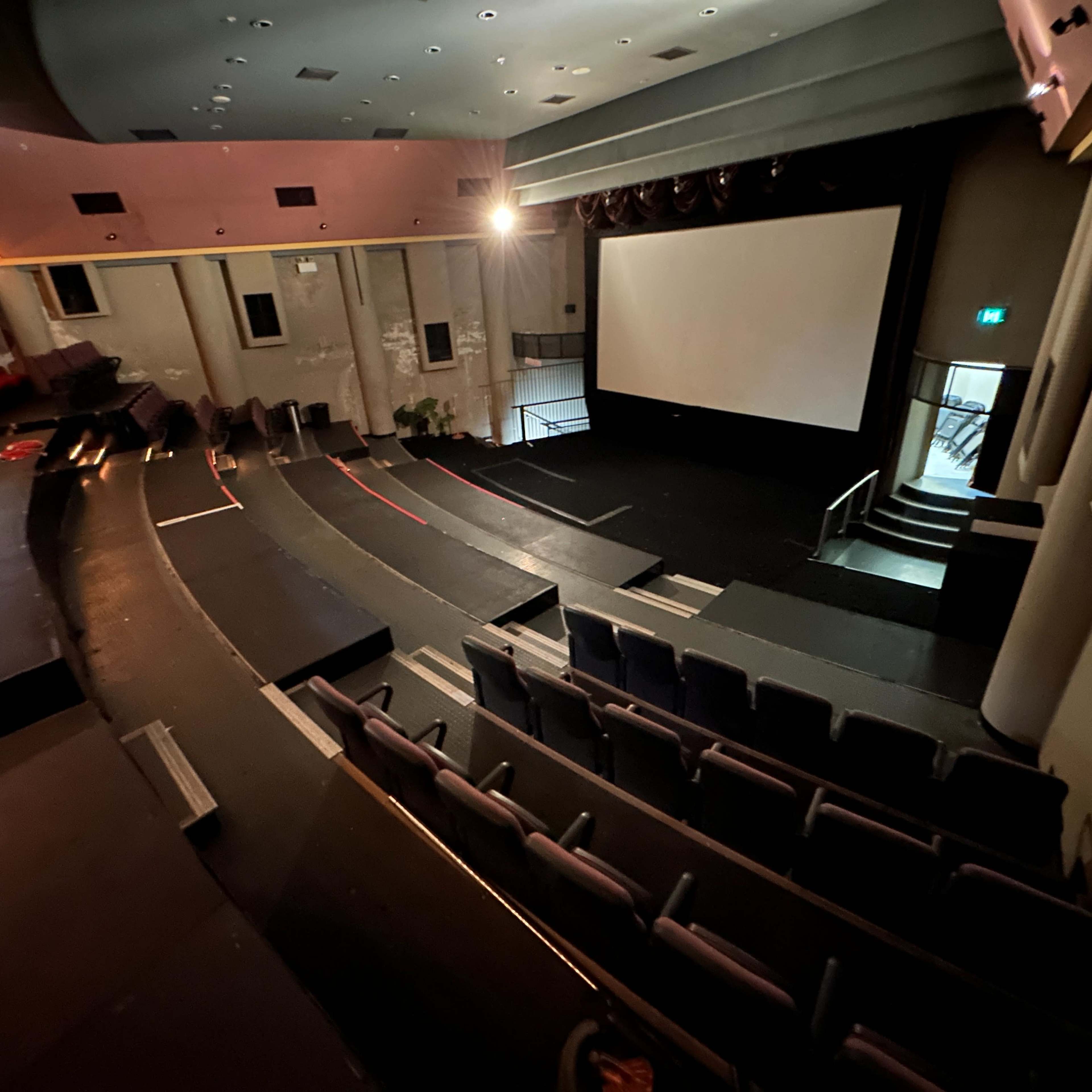 An empty auditorium with tiered seating facing a large screen, illuminated by soft lighting.