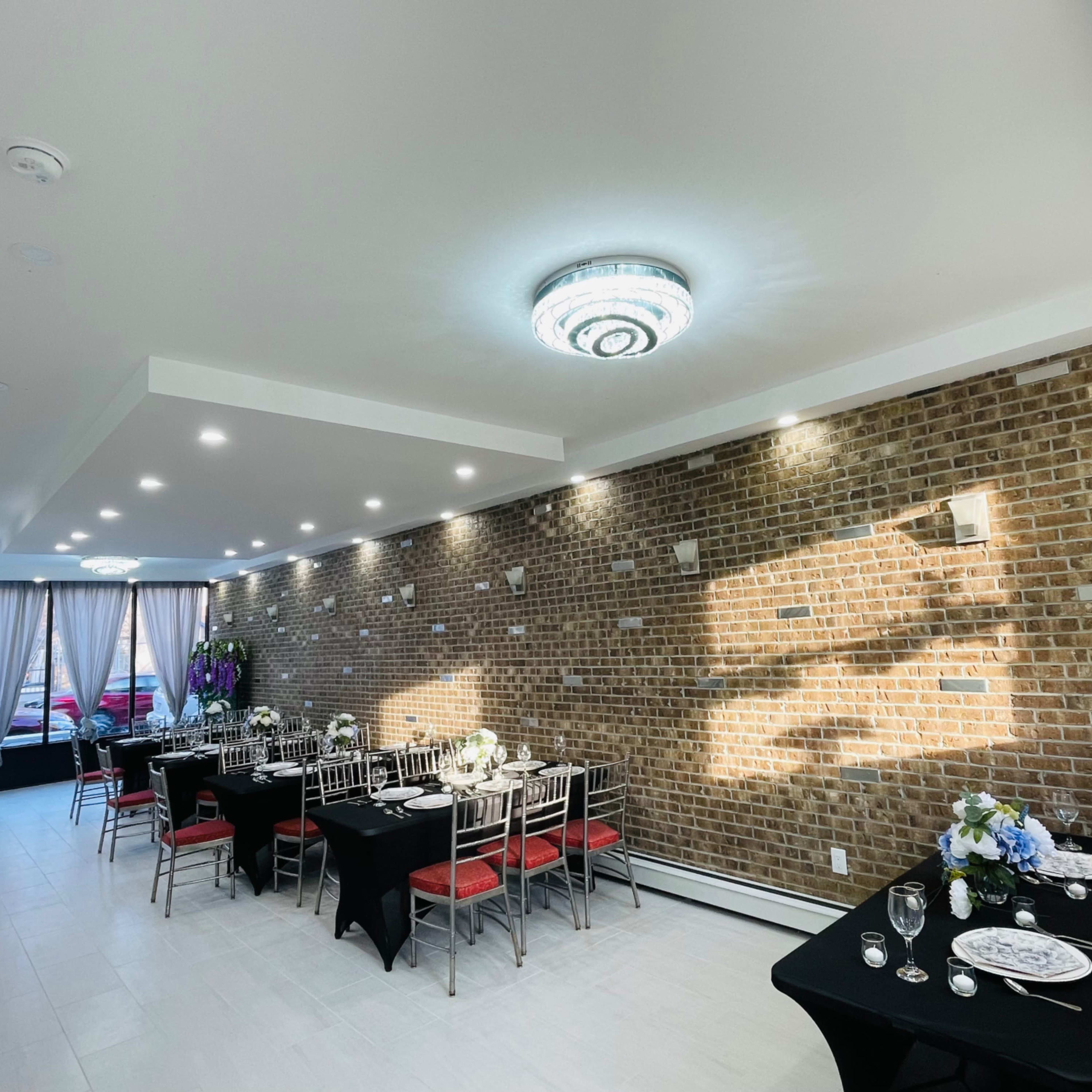 A dining area with two long tables set for a meal, surrounded by brick walls and lit by modern ceiling lights.