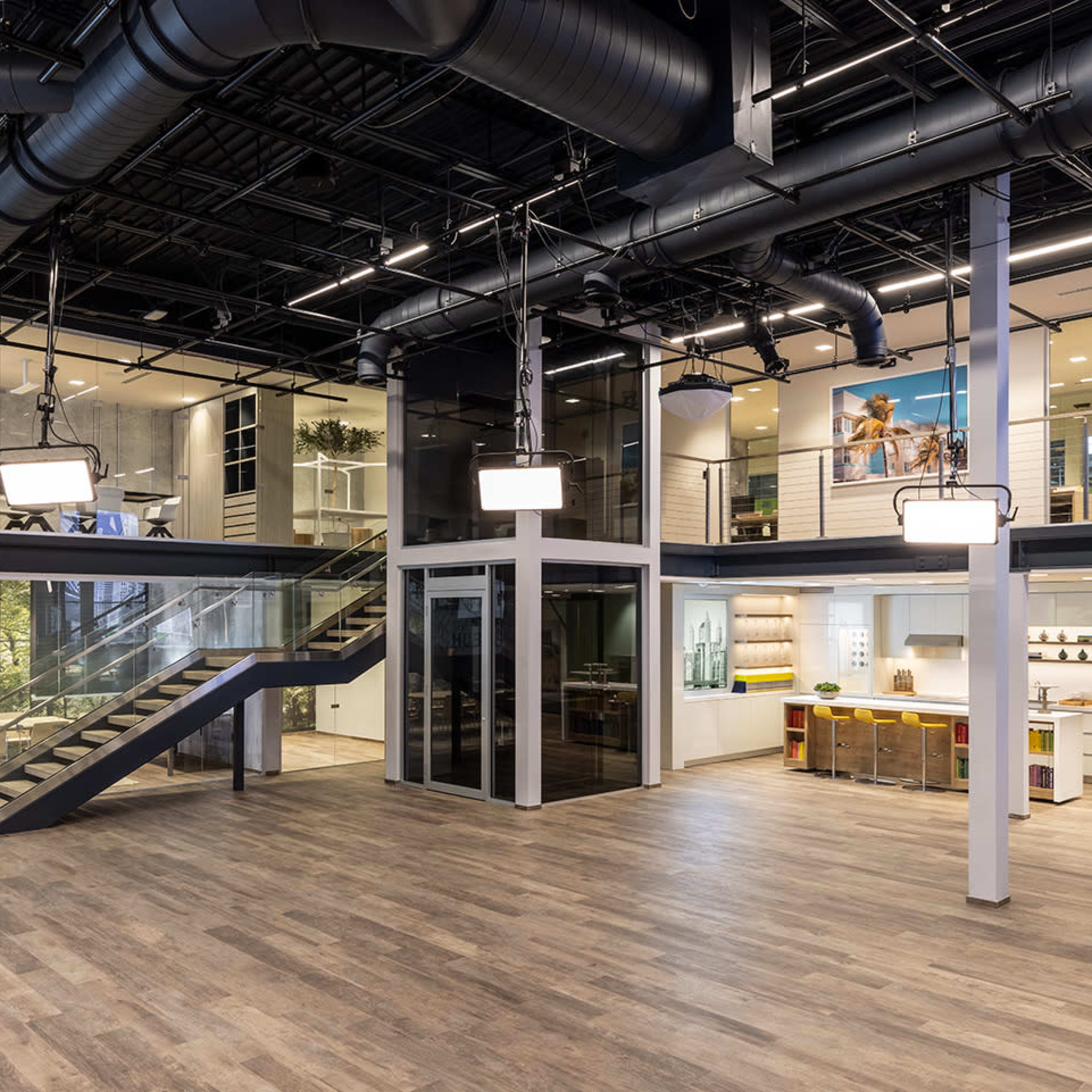 A modern office space with an open layout, featuring a staircase, glass-walled meeting rooms, and areas for collaboration and relaxation.