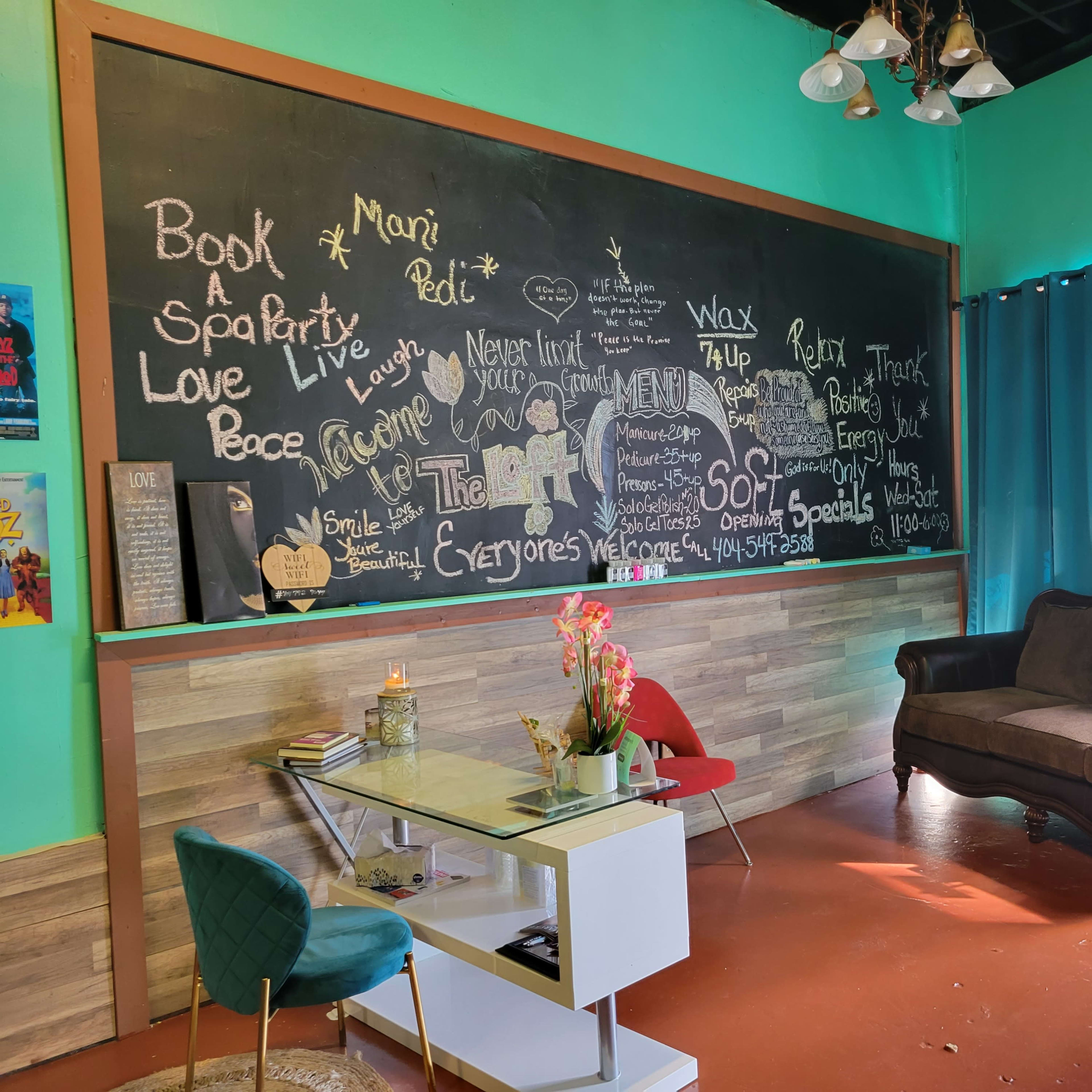 A cozy lounge area with a black chalkboard wall filled with writing, a stylish sofa, a small table, and decorative plants, all set against a vibrant teal background.