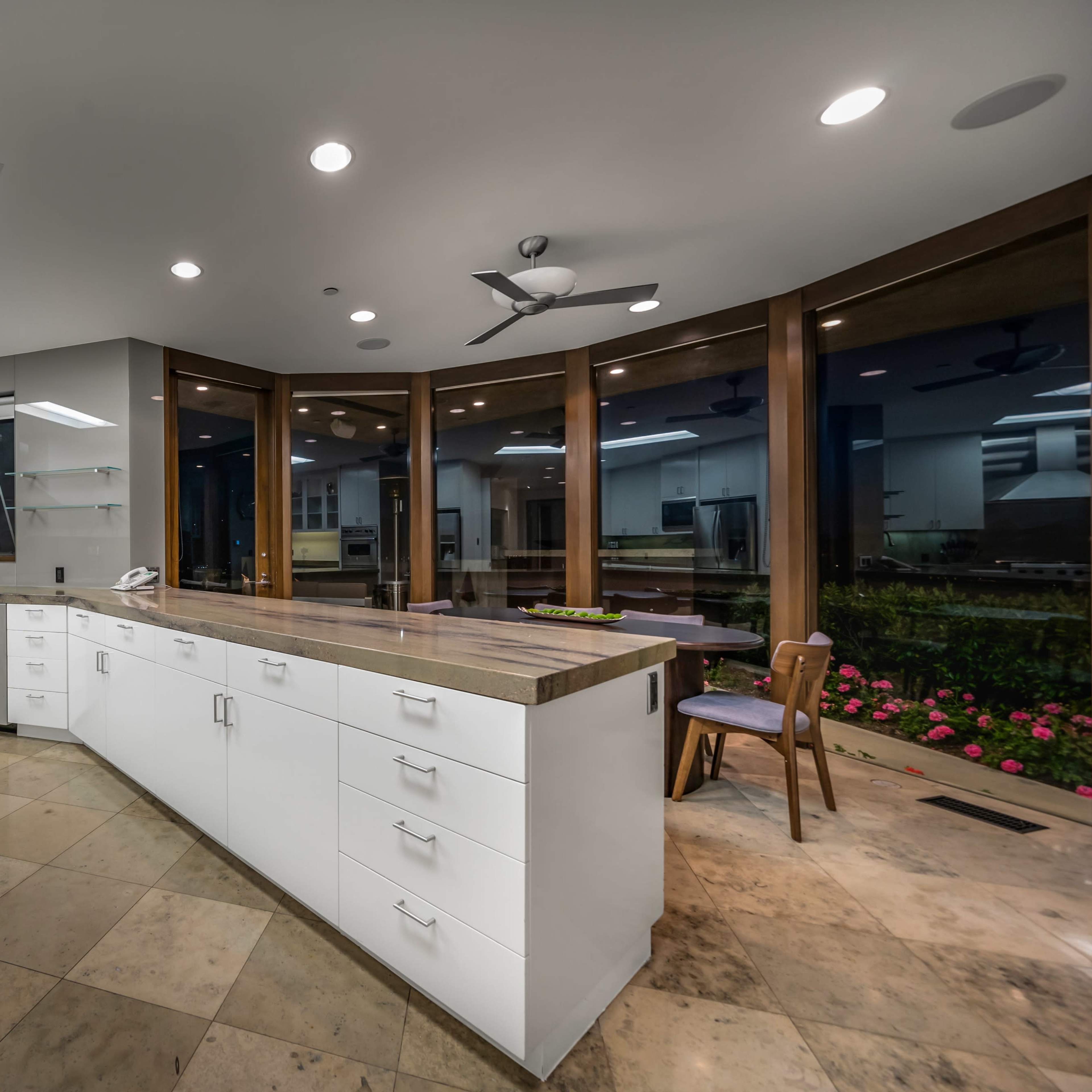 A modern kitchen features white cabinetry, a large central island, and windows overlooking a garden area.