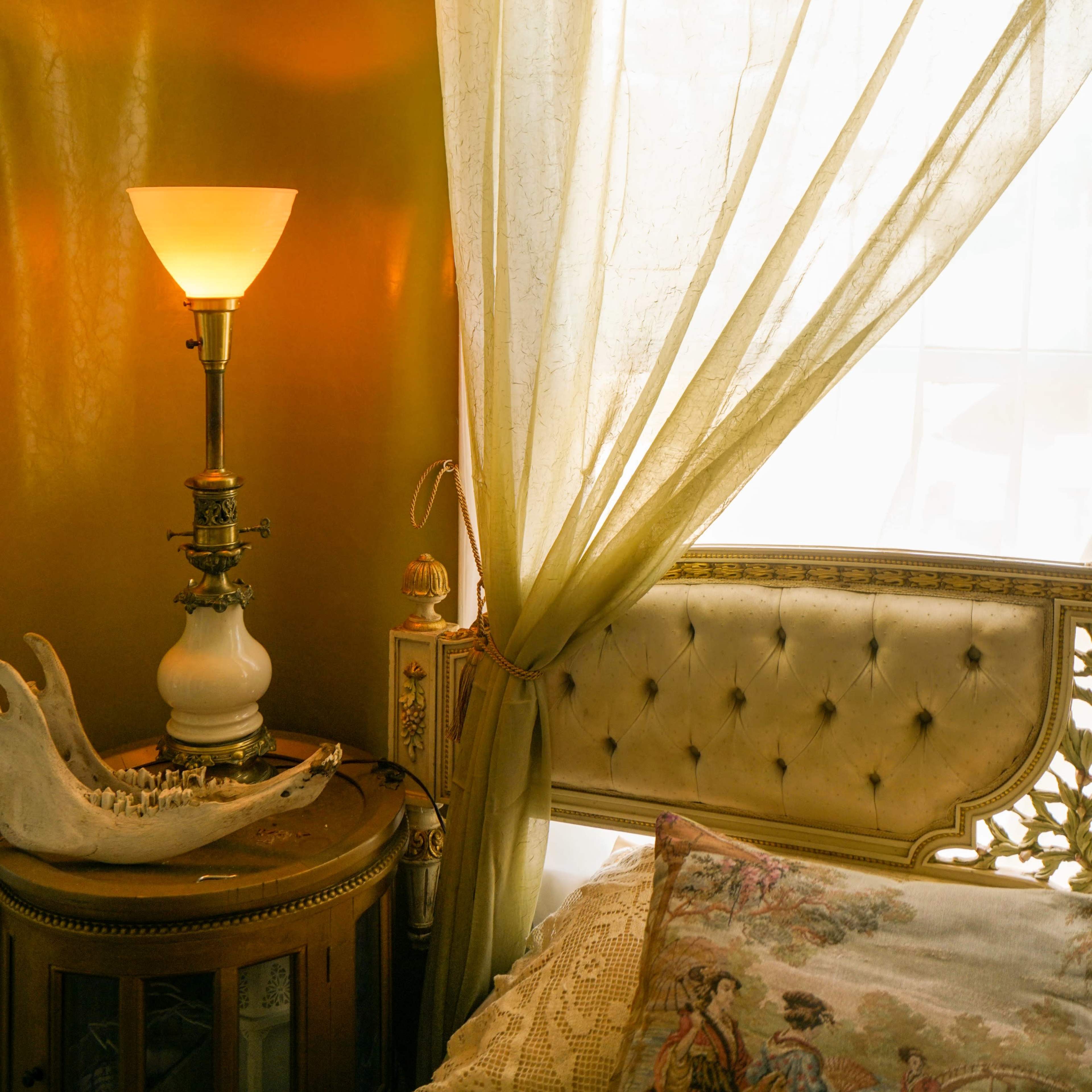 A lamp and a decorative fabric curtain adorn a cozy corner of a bedroom beside a window.