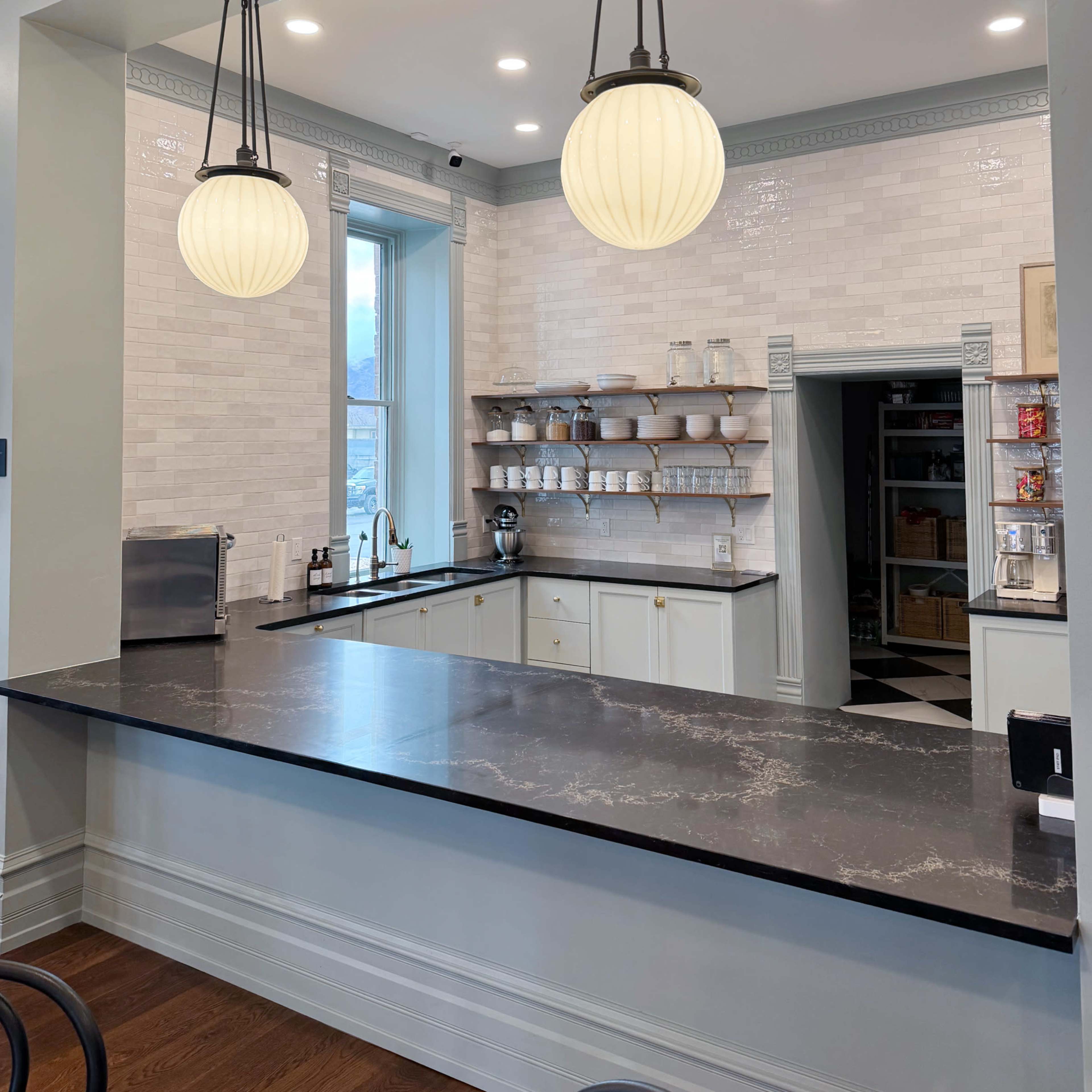 A modern kitchen features a marble countertop, white cabinetry, and large pendant lights hanging above.