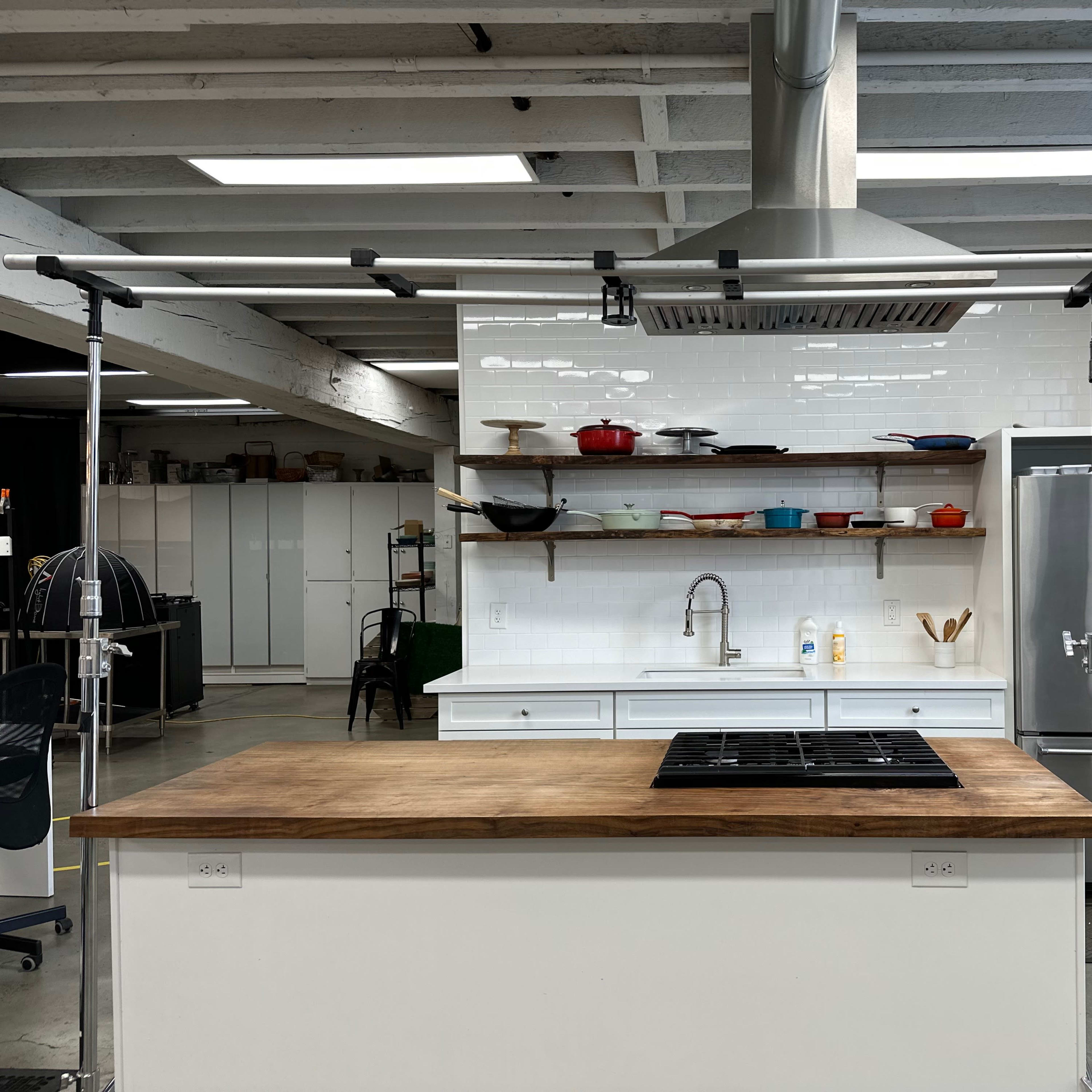A modern kitchen features a central island with a gas cooktop, stainless steel appliances, and open shelving displaying cookware.