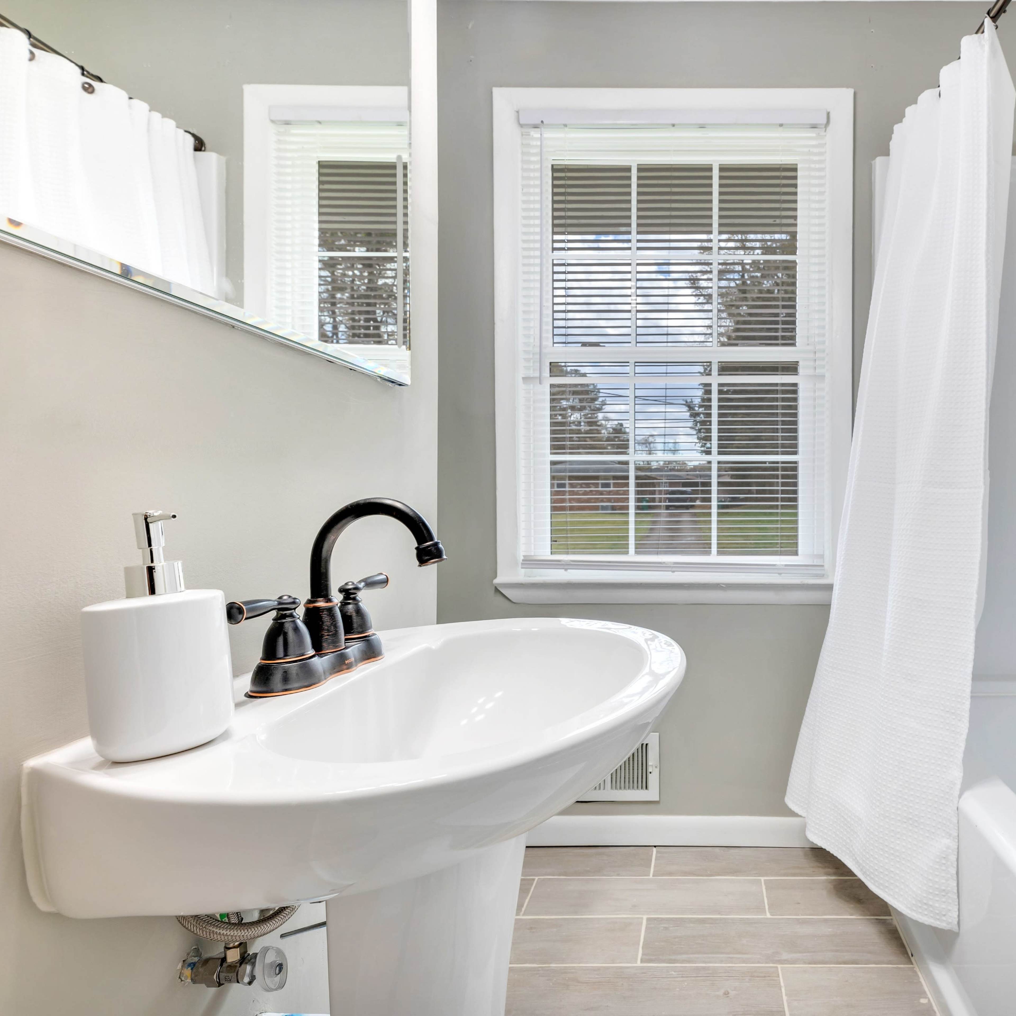 A clean bathroom with a sink, a mirror, a bathtub, and a window with light filtering through.