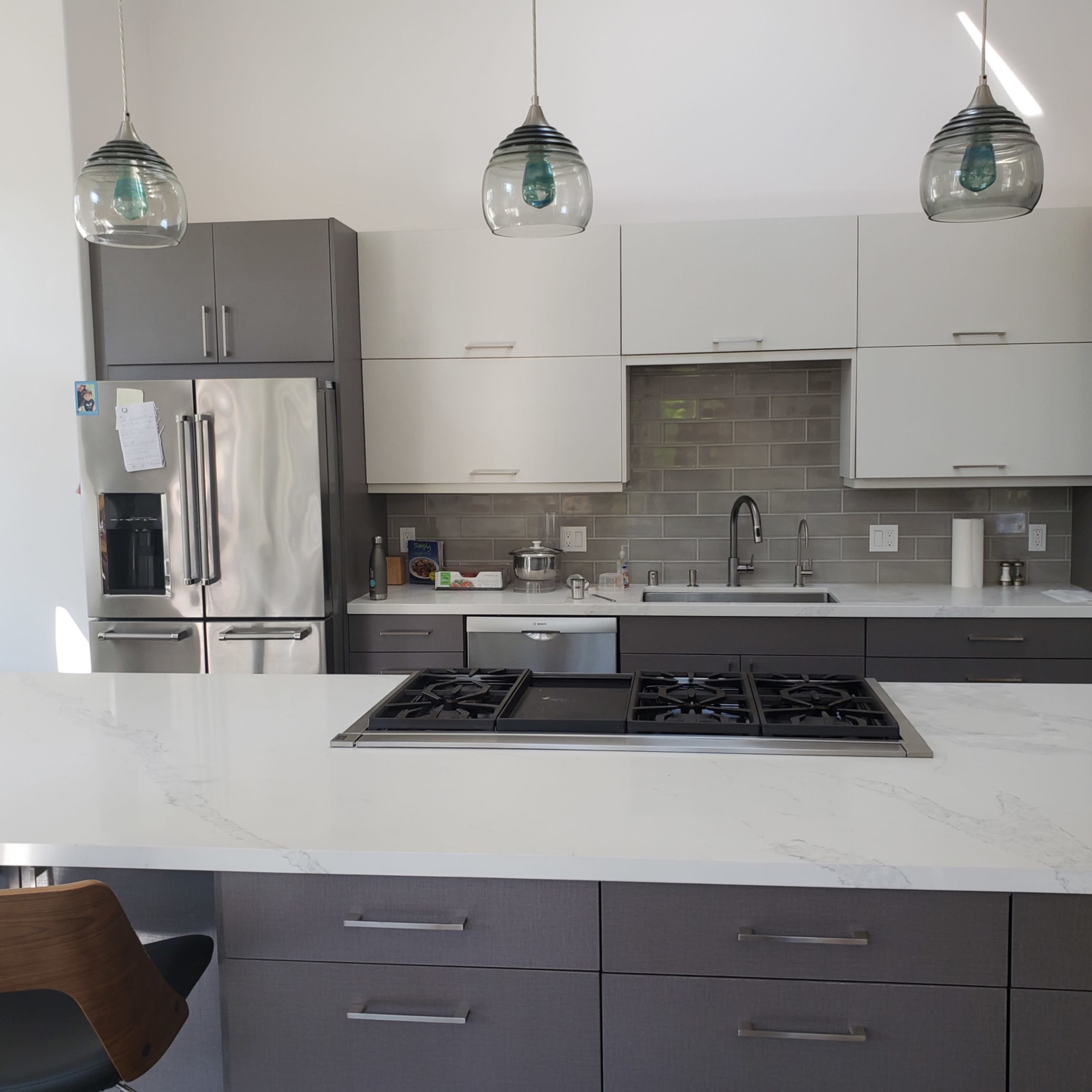 A modern kitchen with gray and white cabinetry, a central island featuring a gas cooktop, and pendant lights hanging above.