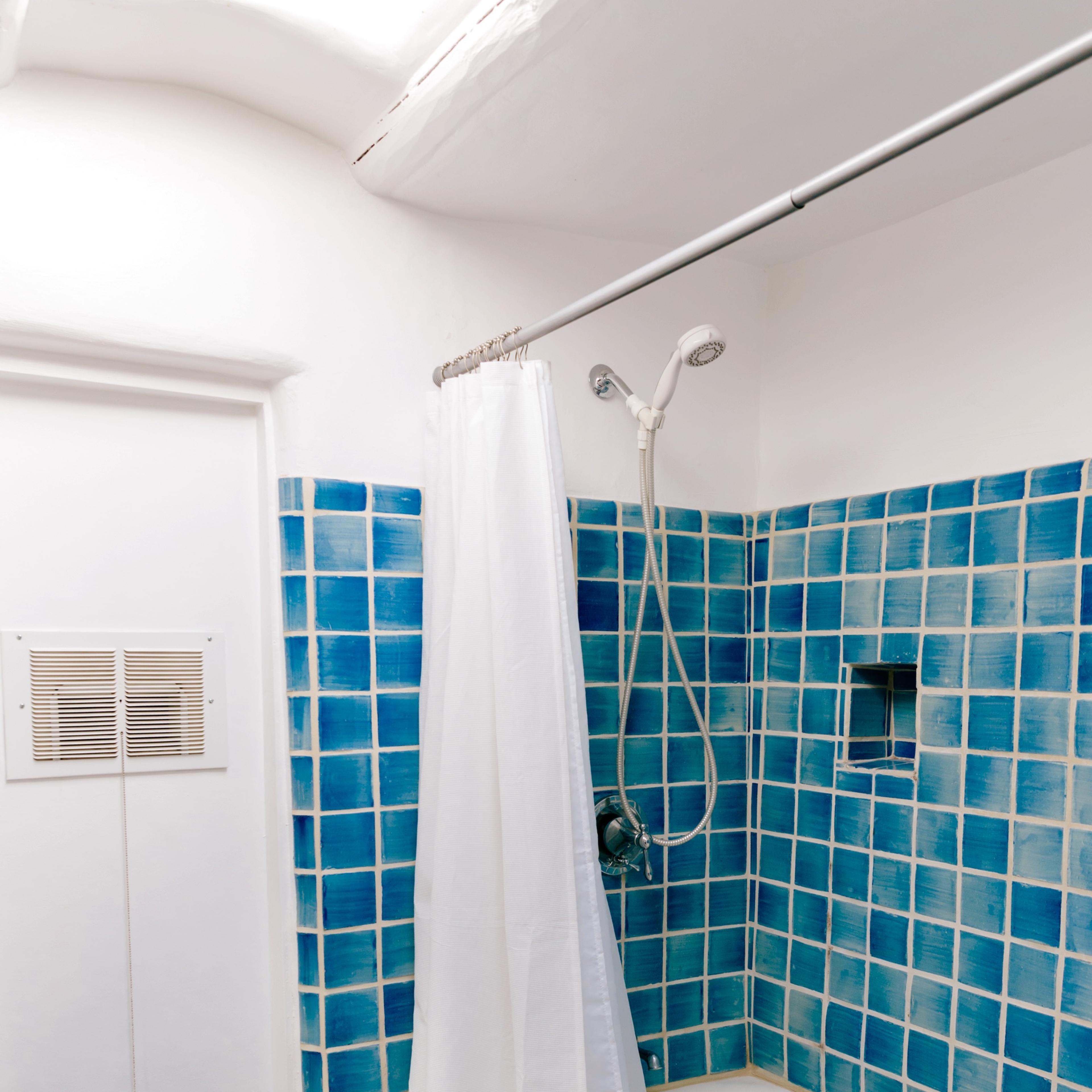 A bathroom featuring a shower with a white curtain and blue tiled walls surrounding a white bathtub.