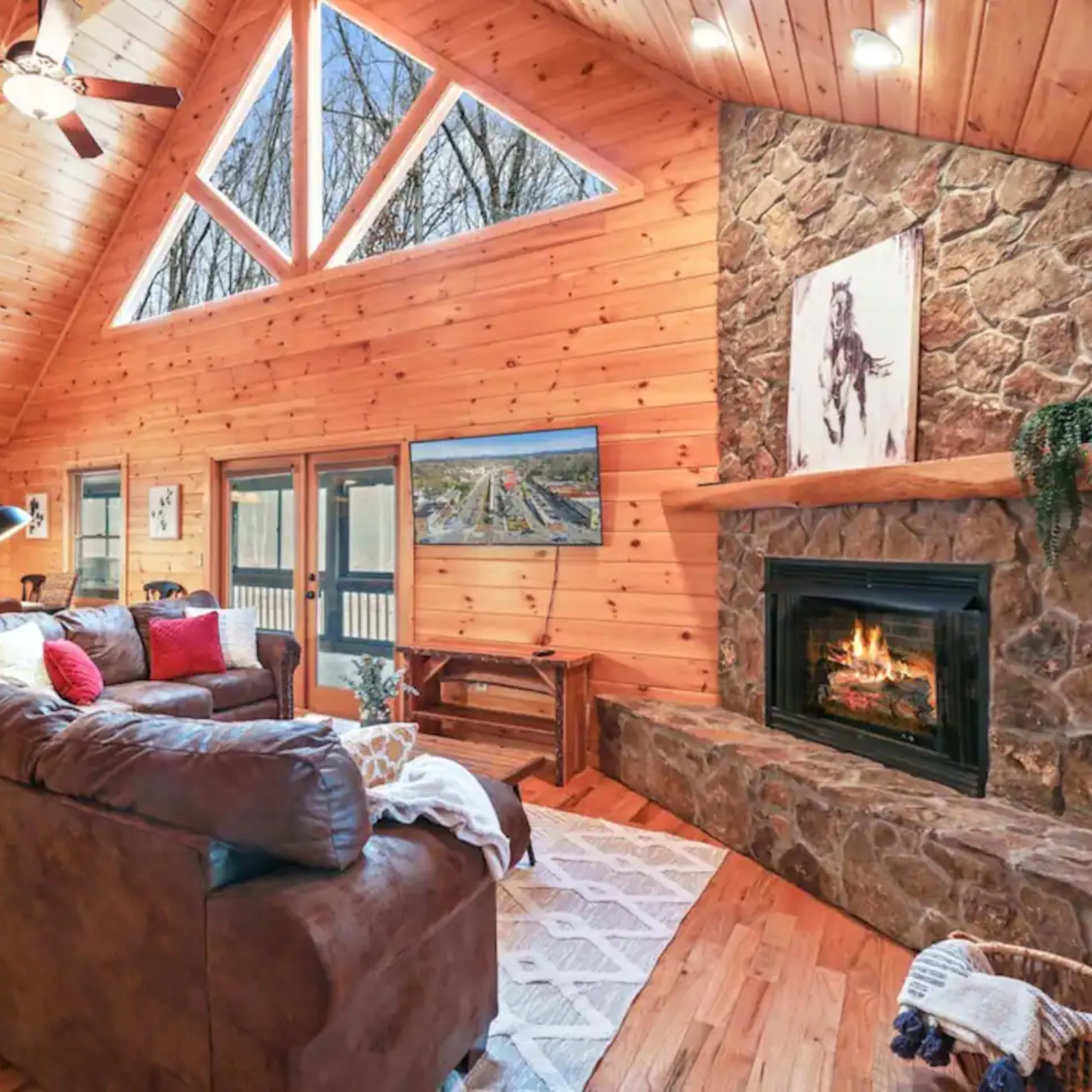 A wooden cabin interior featuring a living area with a stone fireplace, large windows, and a sectional sofa.