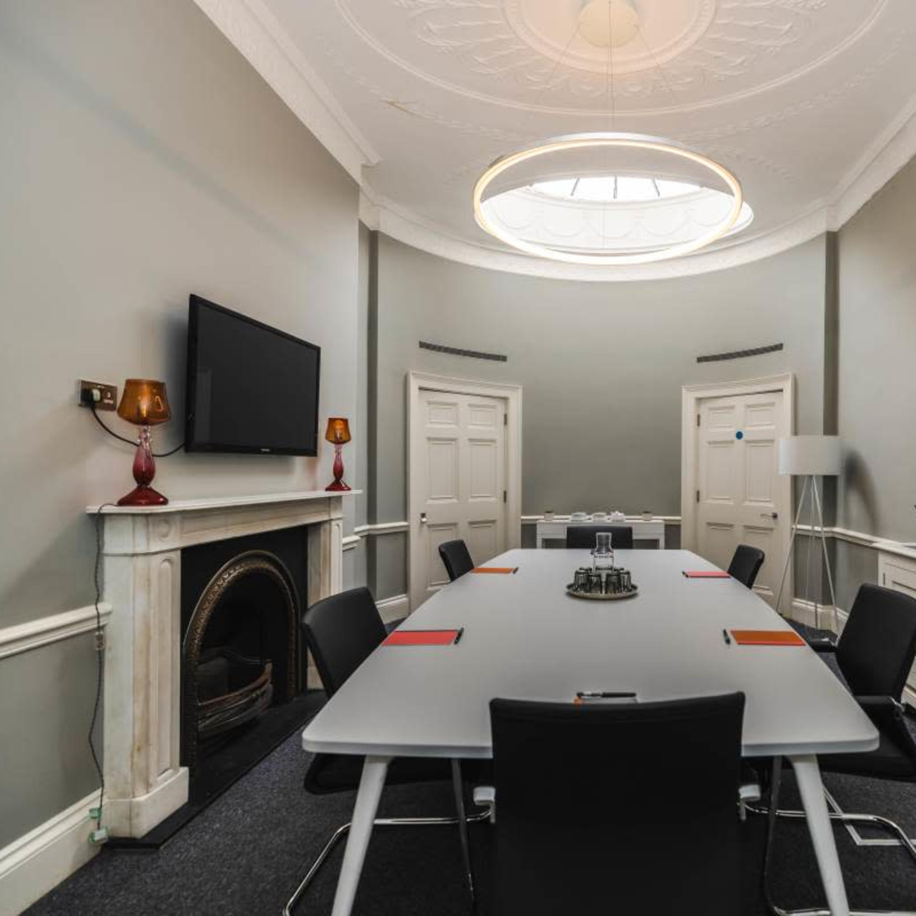 A modern conference room featuring a long table surrounded by black chairs, a wall-mounted television, and a decorative fireplace.