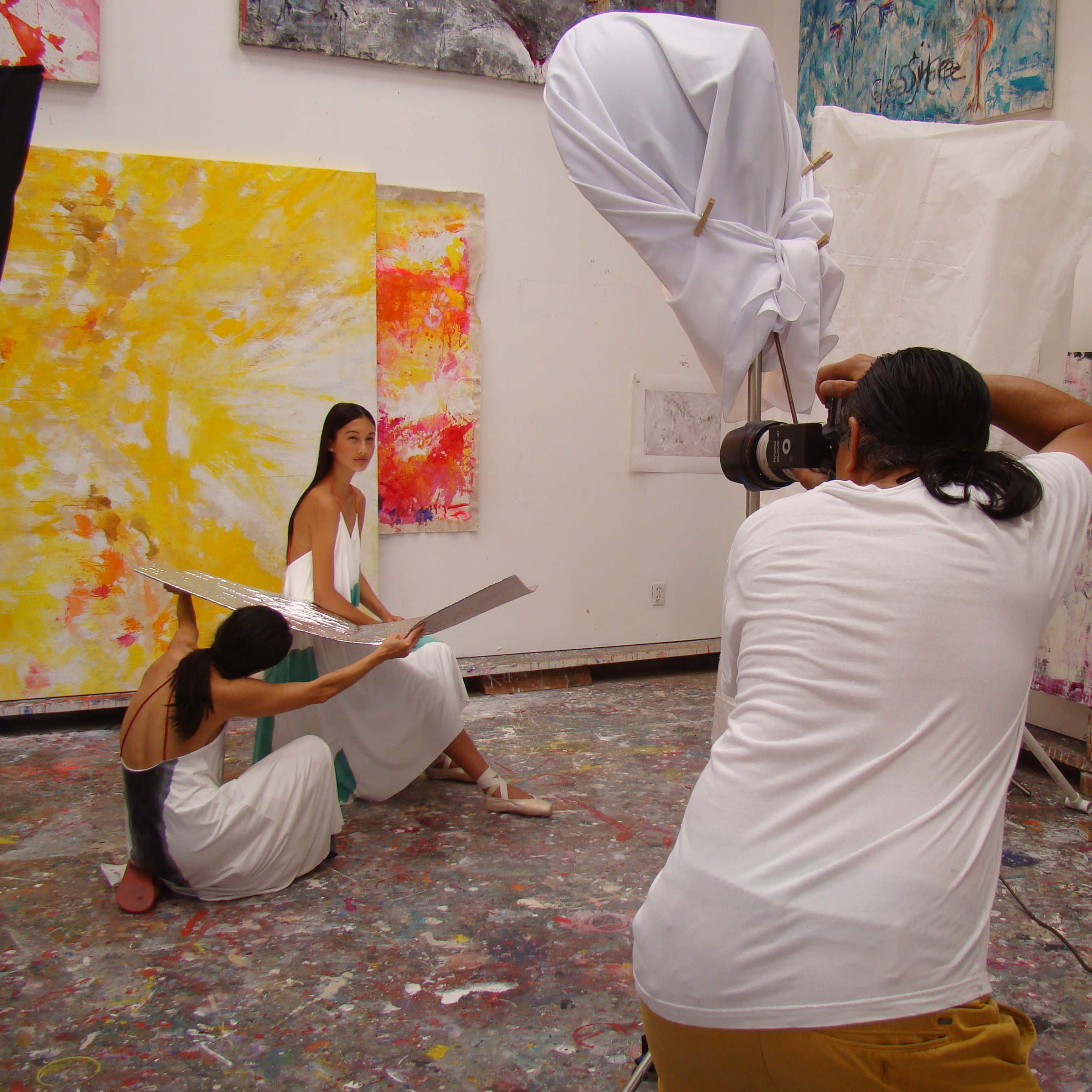 A spacious artist's studio with large skylights, colorful paintings on the walls, and scattered art supplies on the floor.