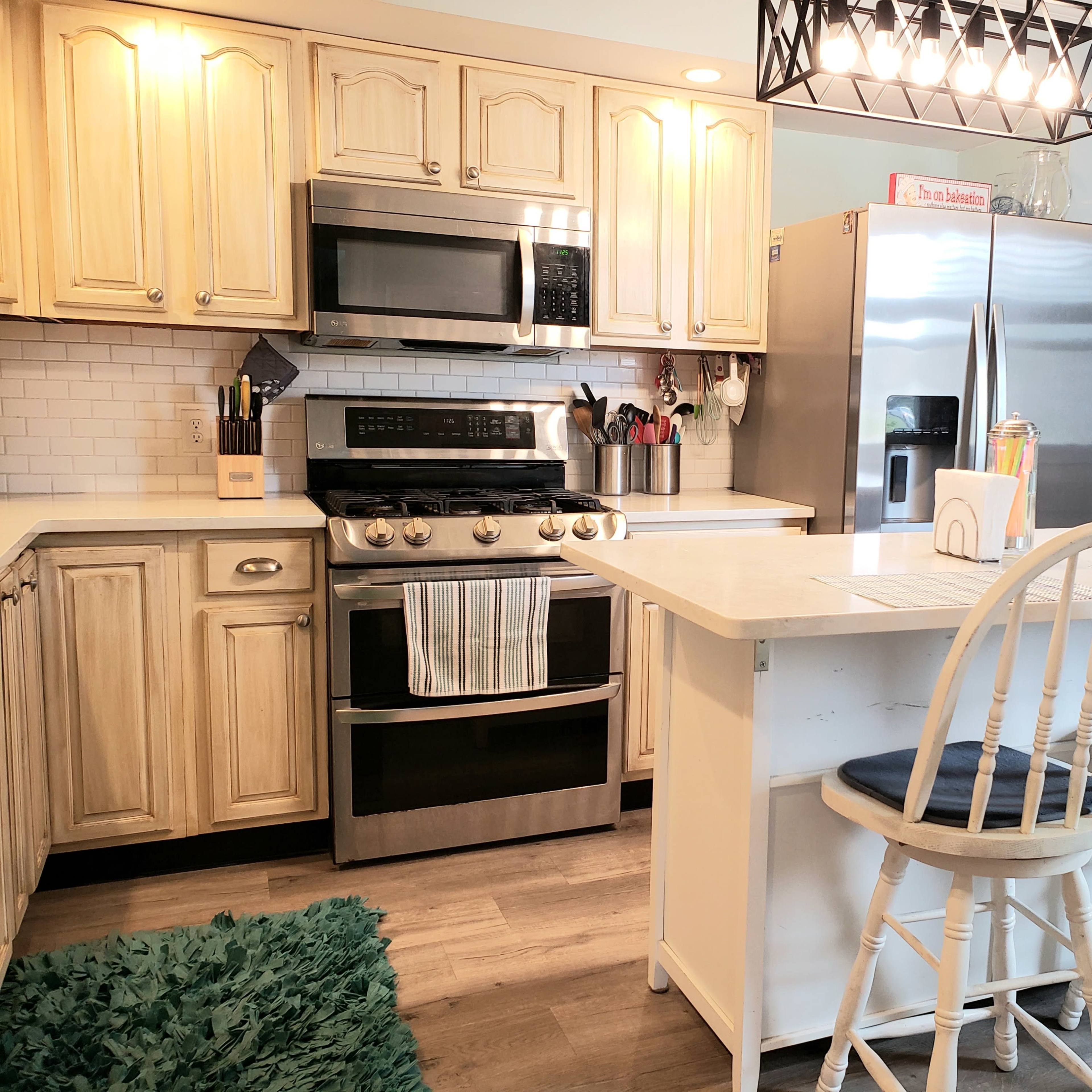 A modern kitchen with light wood cabinets, stainless steel appliances, and a central island with two white bar stools.