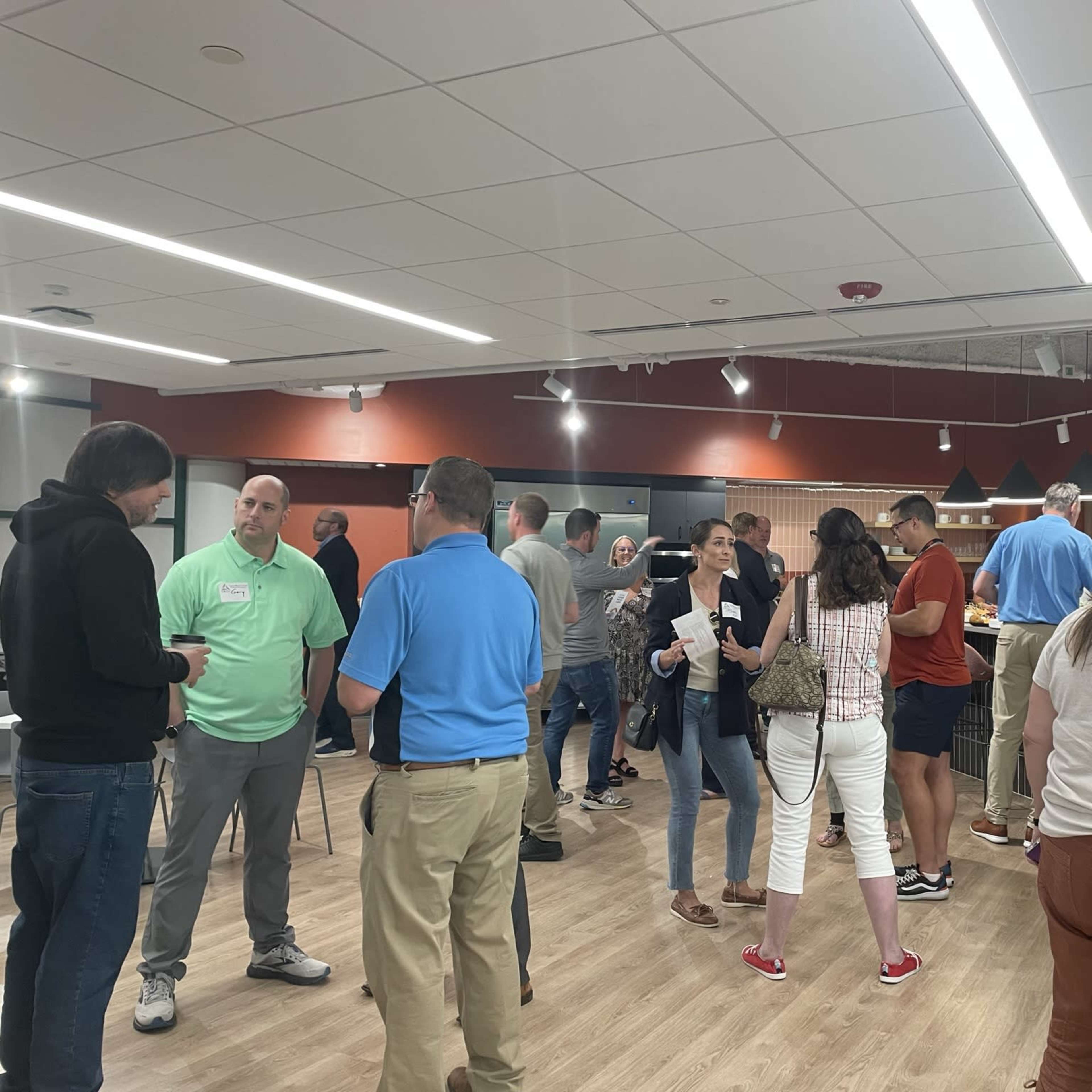 A group of people is engaged in conversation at a social gathering in a modern indoor space with tables and chairs.