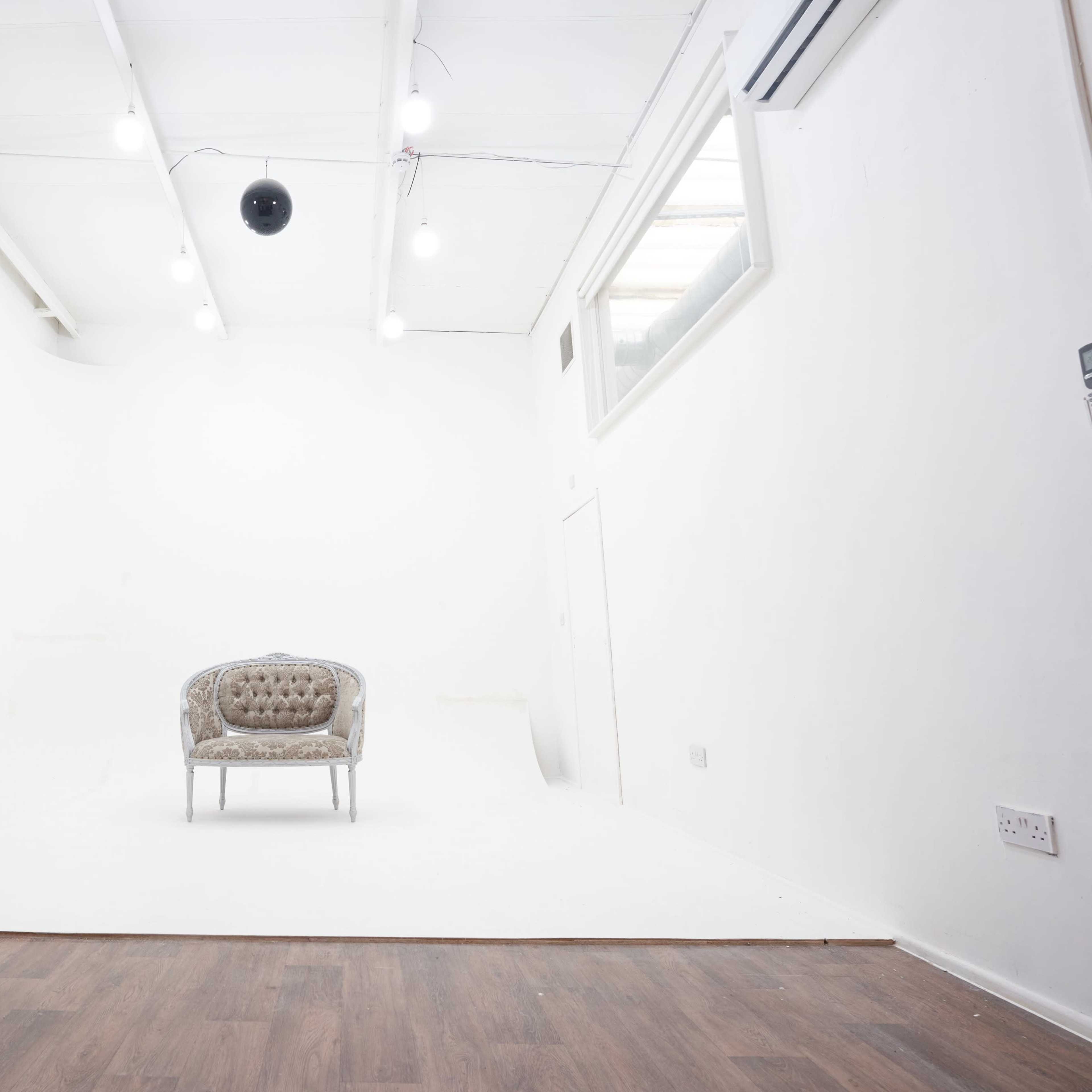 A minimalist studio space with a single tufted chair on a white backdrop and overhead lighting.