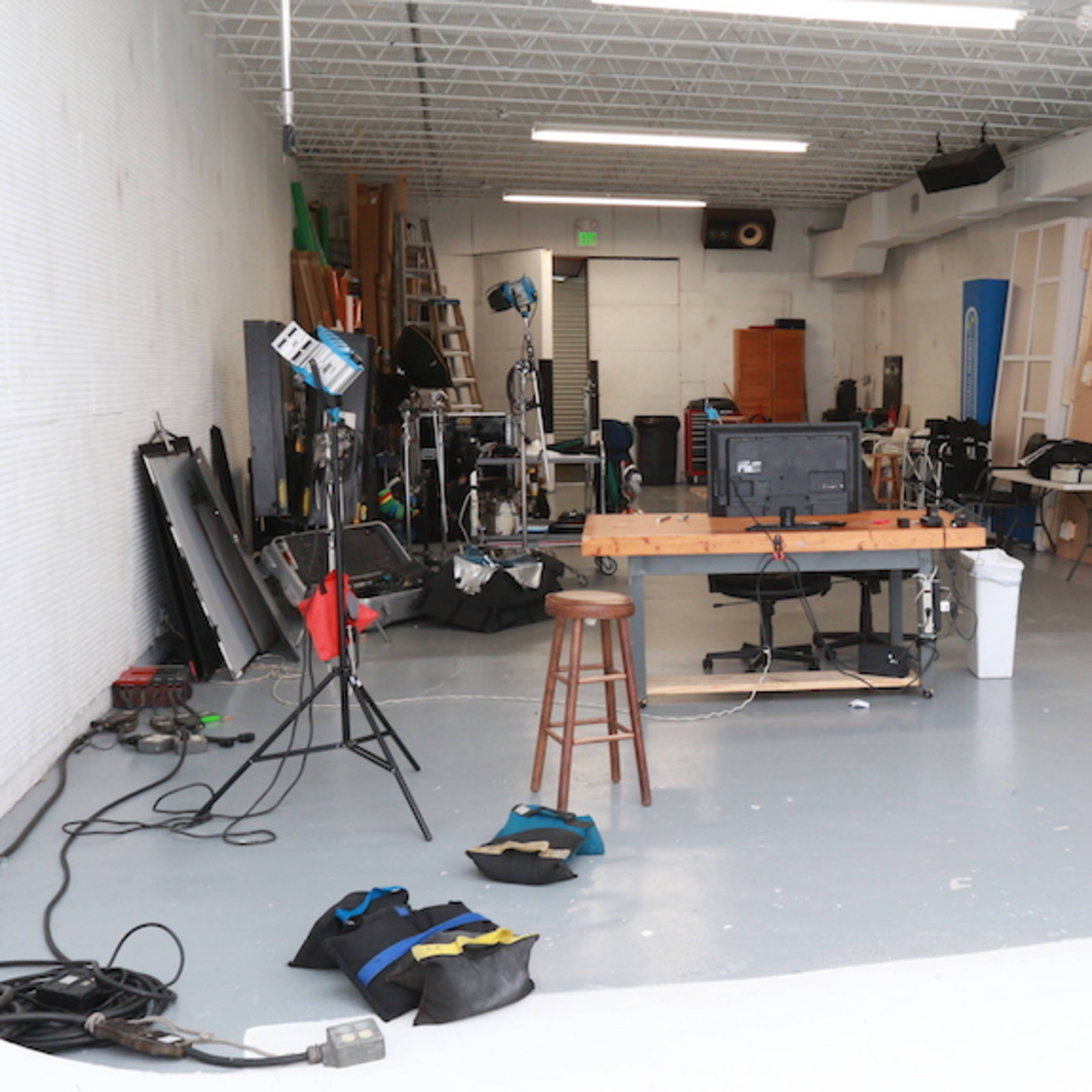 A photography studio with various equipment, including lighting stands and a work table, arranged in a spacious environment.