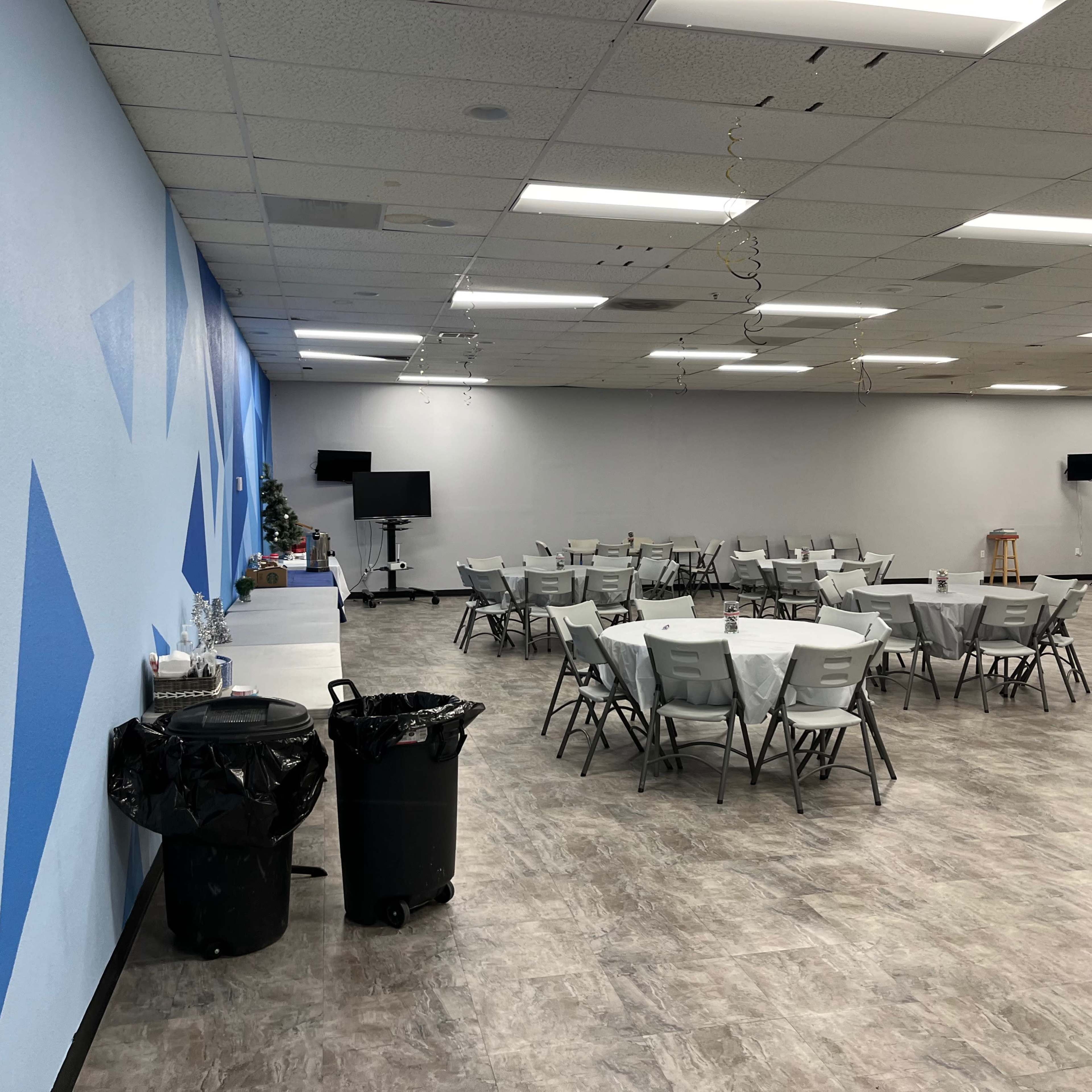 A large room with gray flooring, multiple tables set with white tablecloths, and blue painted walls featuring geometric designs.
