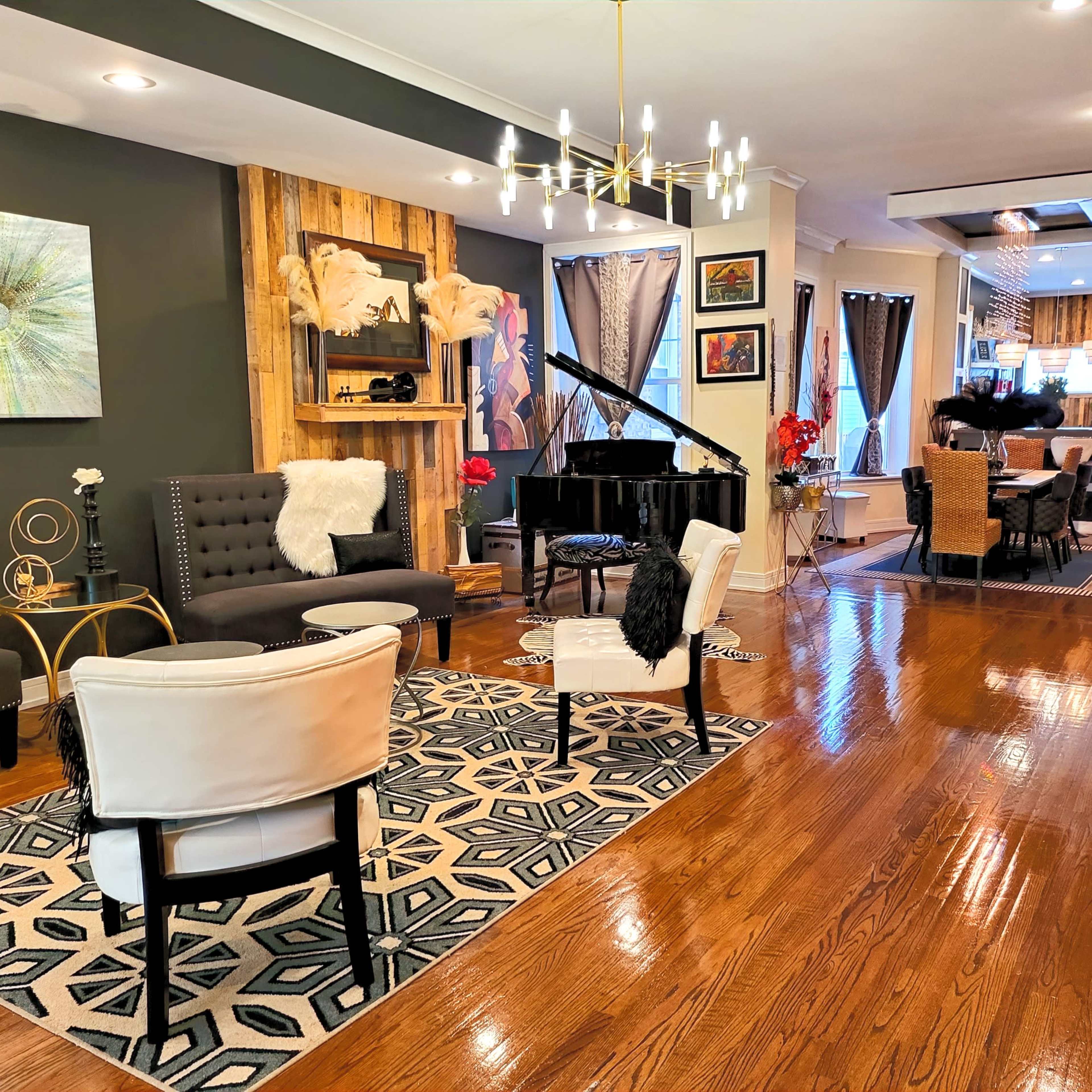 A spacious living area features a black grand piano, assorted seating, and a decorative fireplace with contemporary art on the walls.