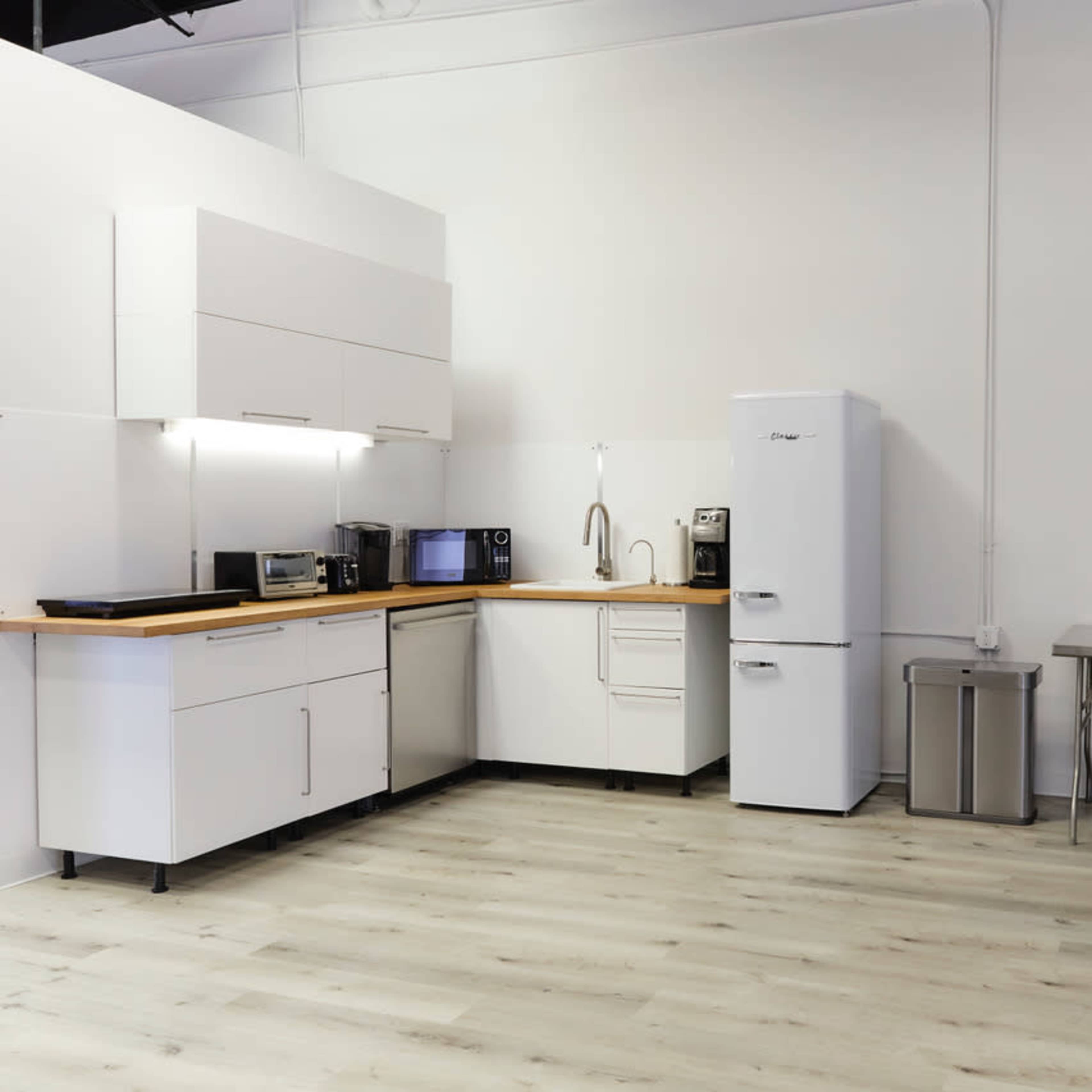A modern kitchen with white cabinetry, a stainless steel table, and various appliances including a microwave and refrigerator.