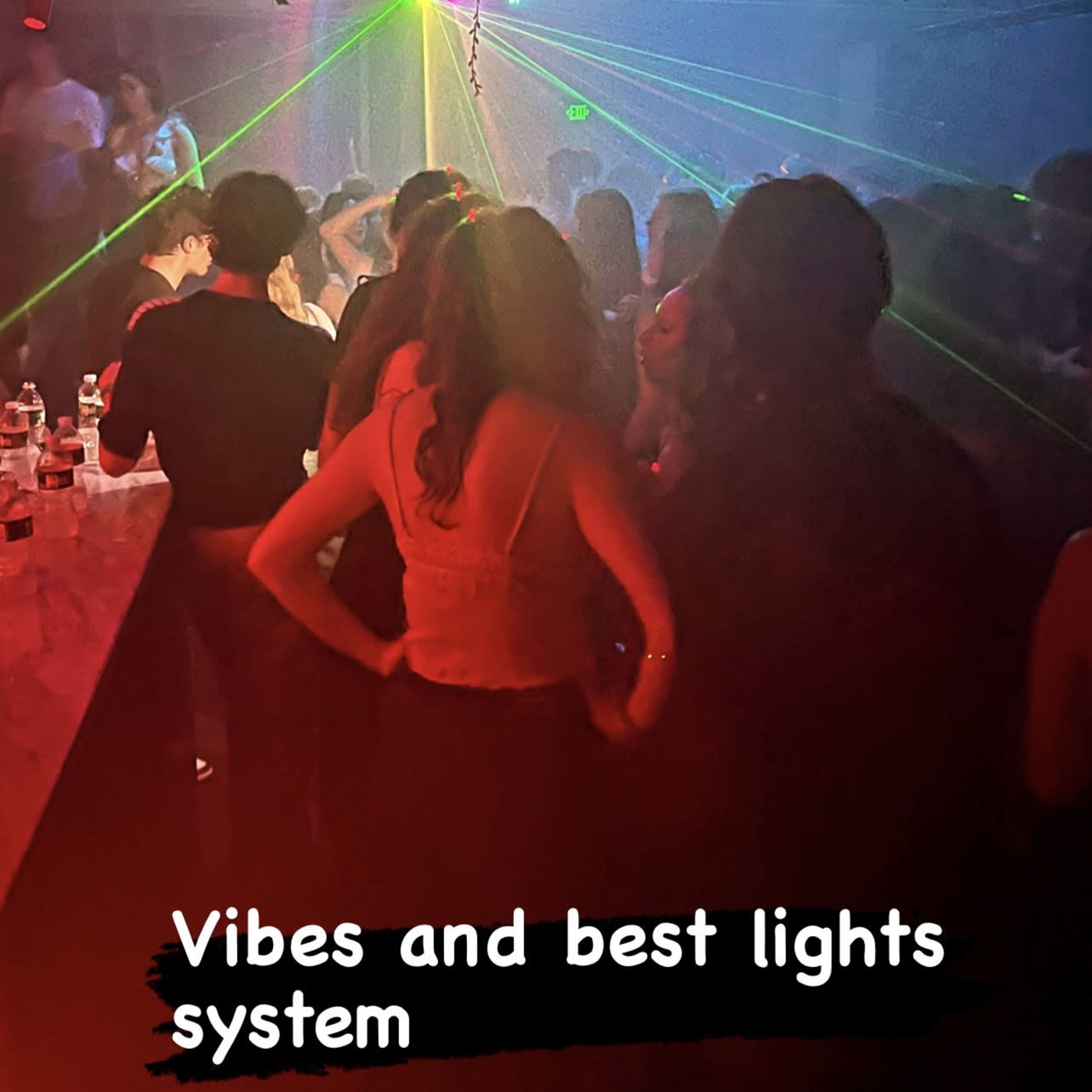 A group of people socialize in a dimly lit venue with colorful laser lights illuminating the space.