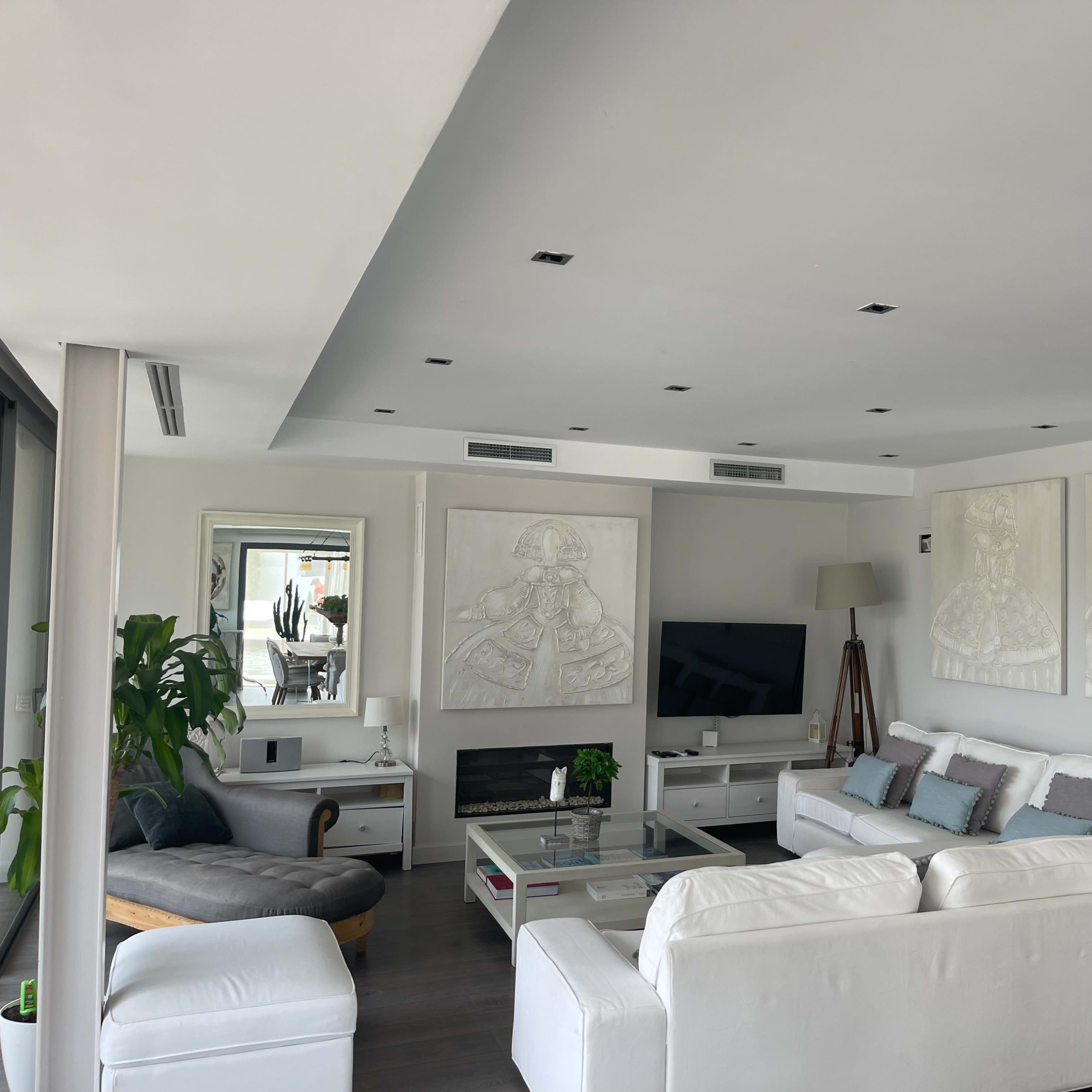 A modern living room features white furniture, two large wall art pieces, and a television mounted above a fireplace.