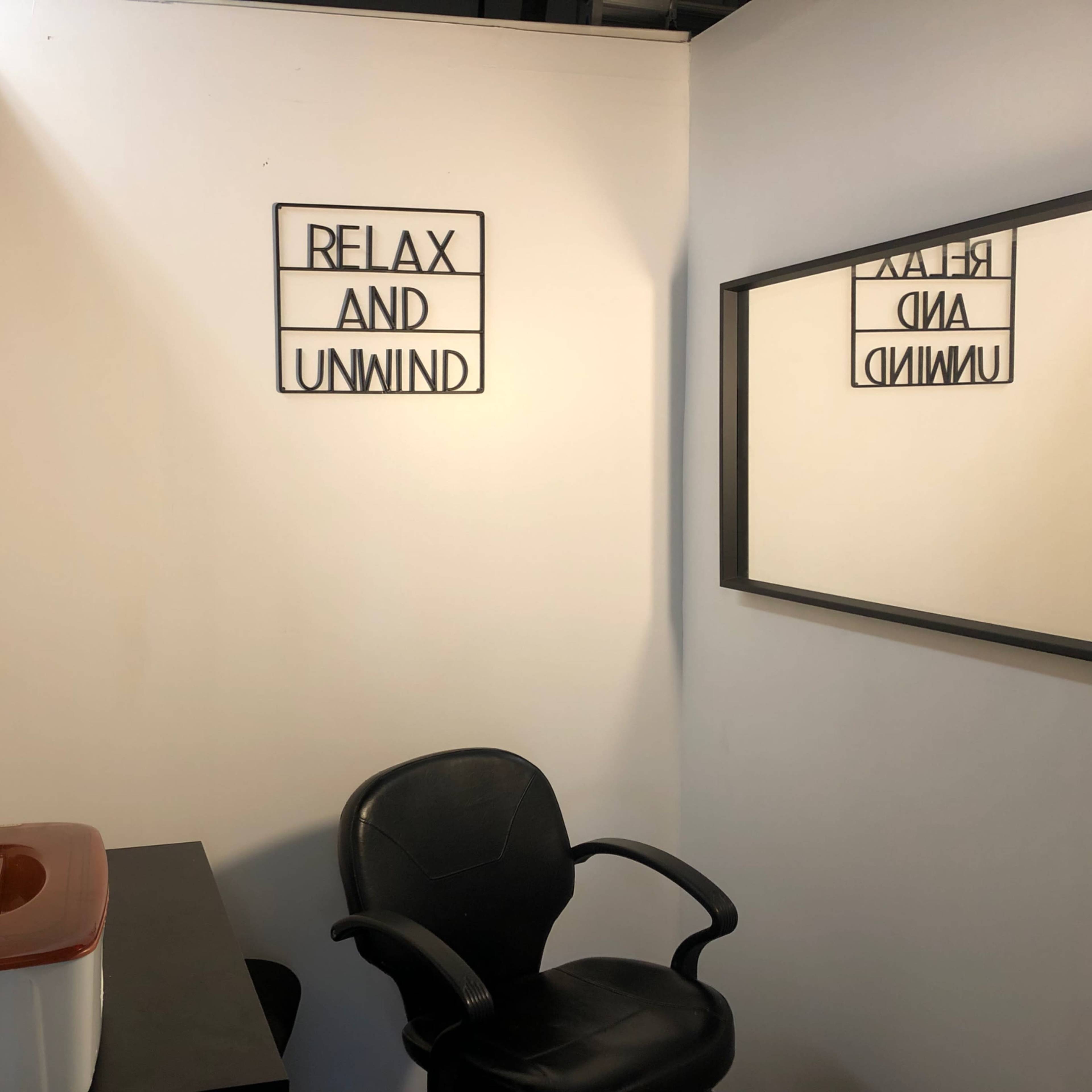 A small room with a black chair, a tabletop, a foot spa, a mirror, and a sign that reads "RELAX AND UNWIND."