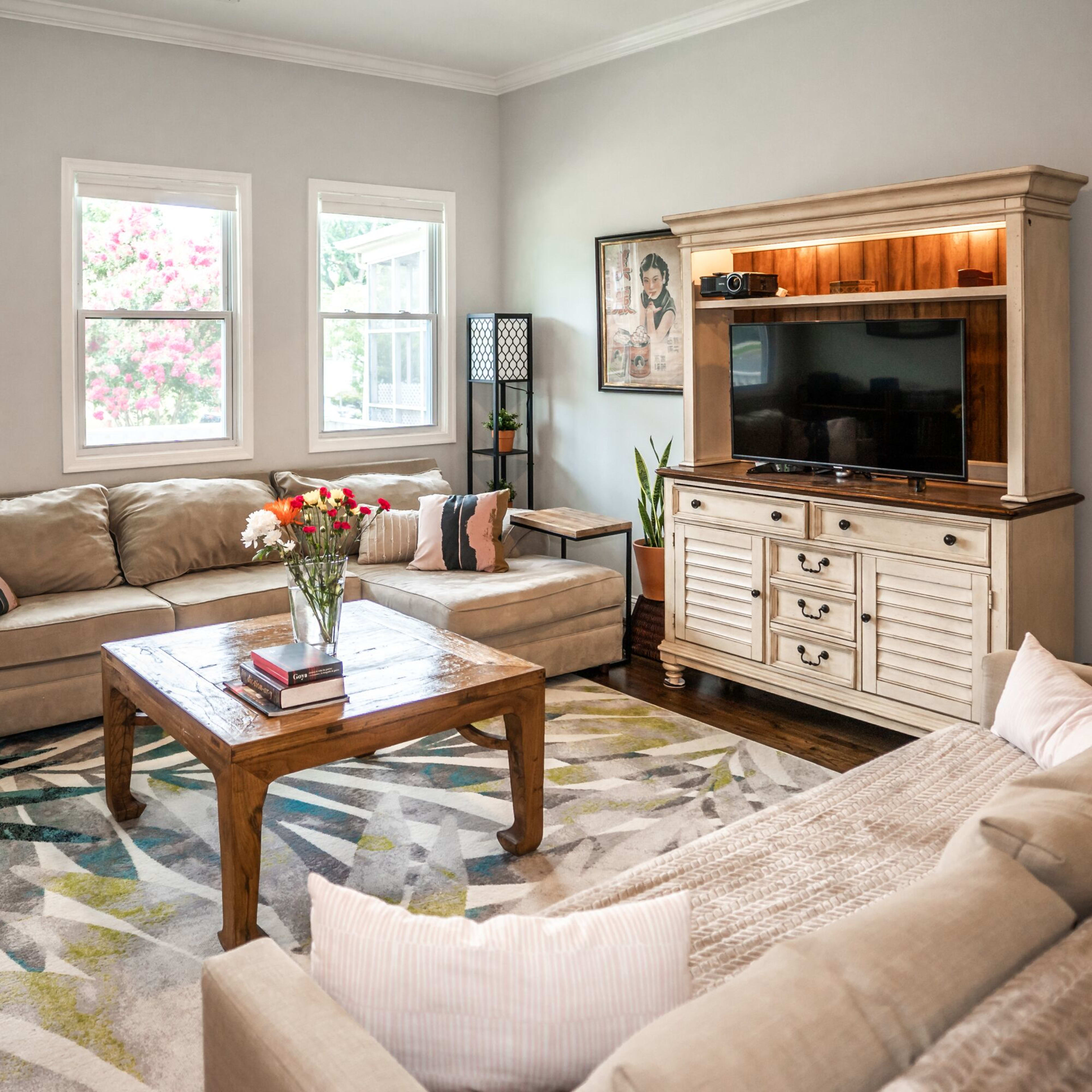 The living room features a beige sectional sofa, a wooden coffee table, and a media console with a television, all arranged around a patterned area rug.