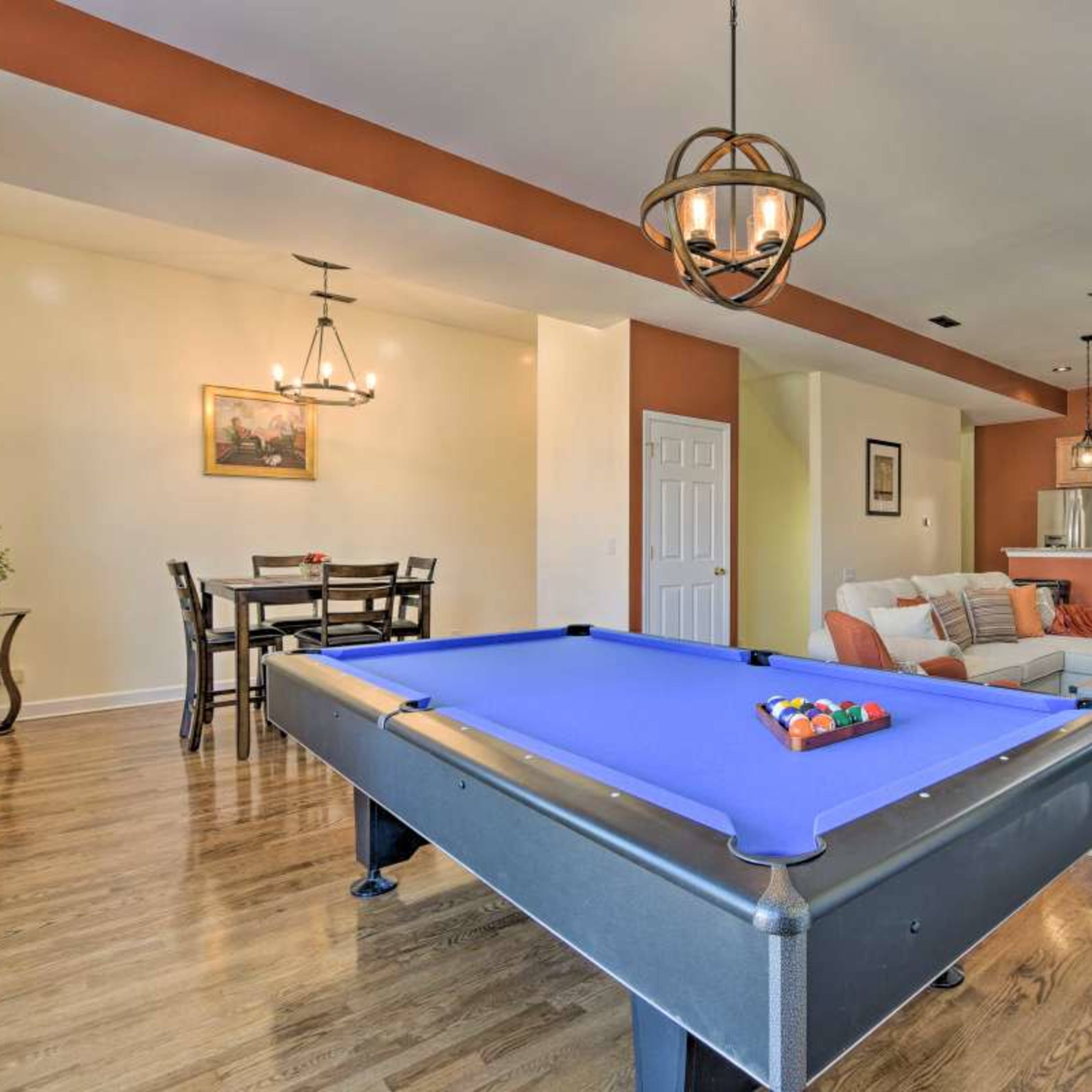 A modern living space with a pool table in the foreground, a dining area with a table and chairs, and a kitchen visible in the background.