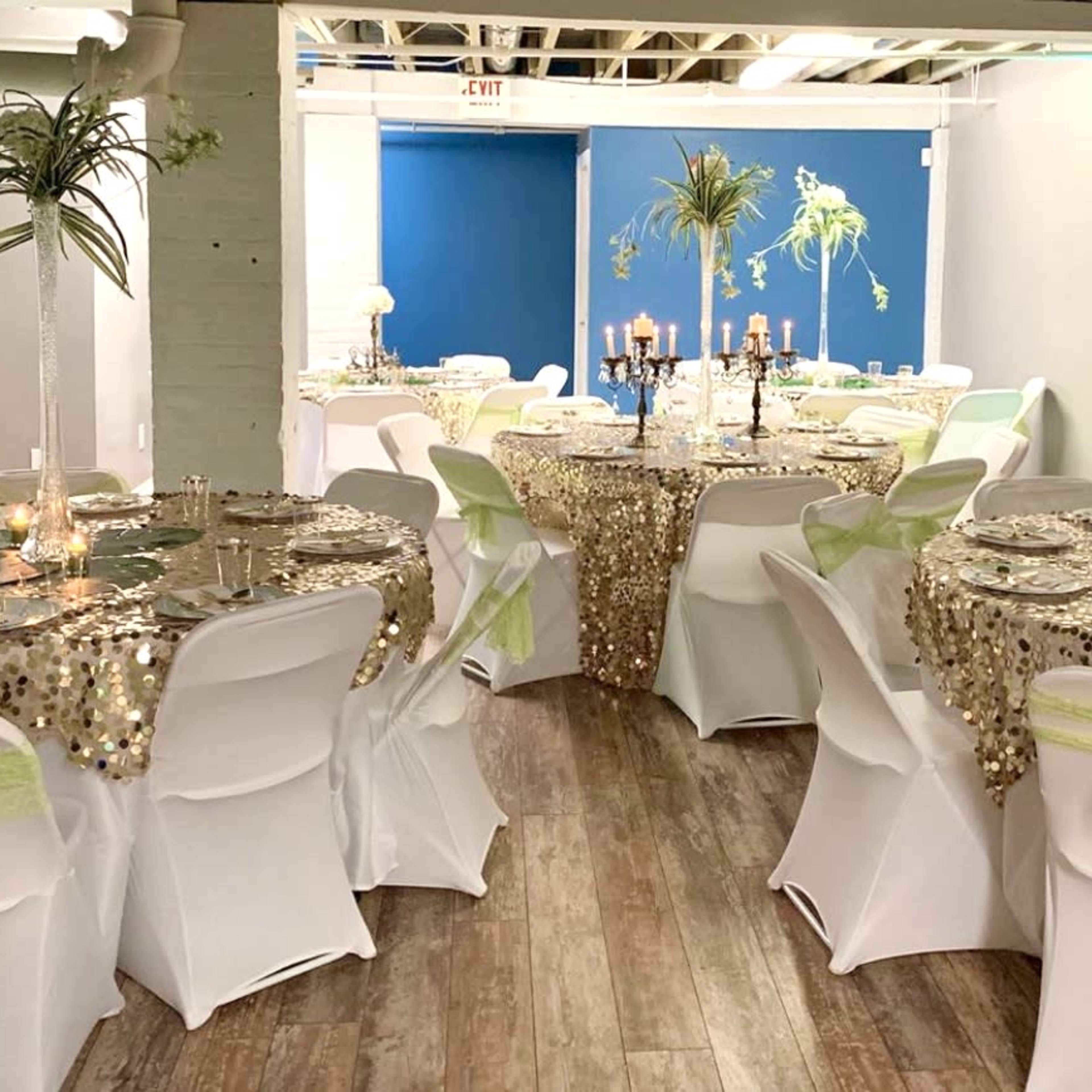 A decorated event space with elegantly arranged tables covered in sequin tablecloths, adorned with candles and centerpieces.