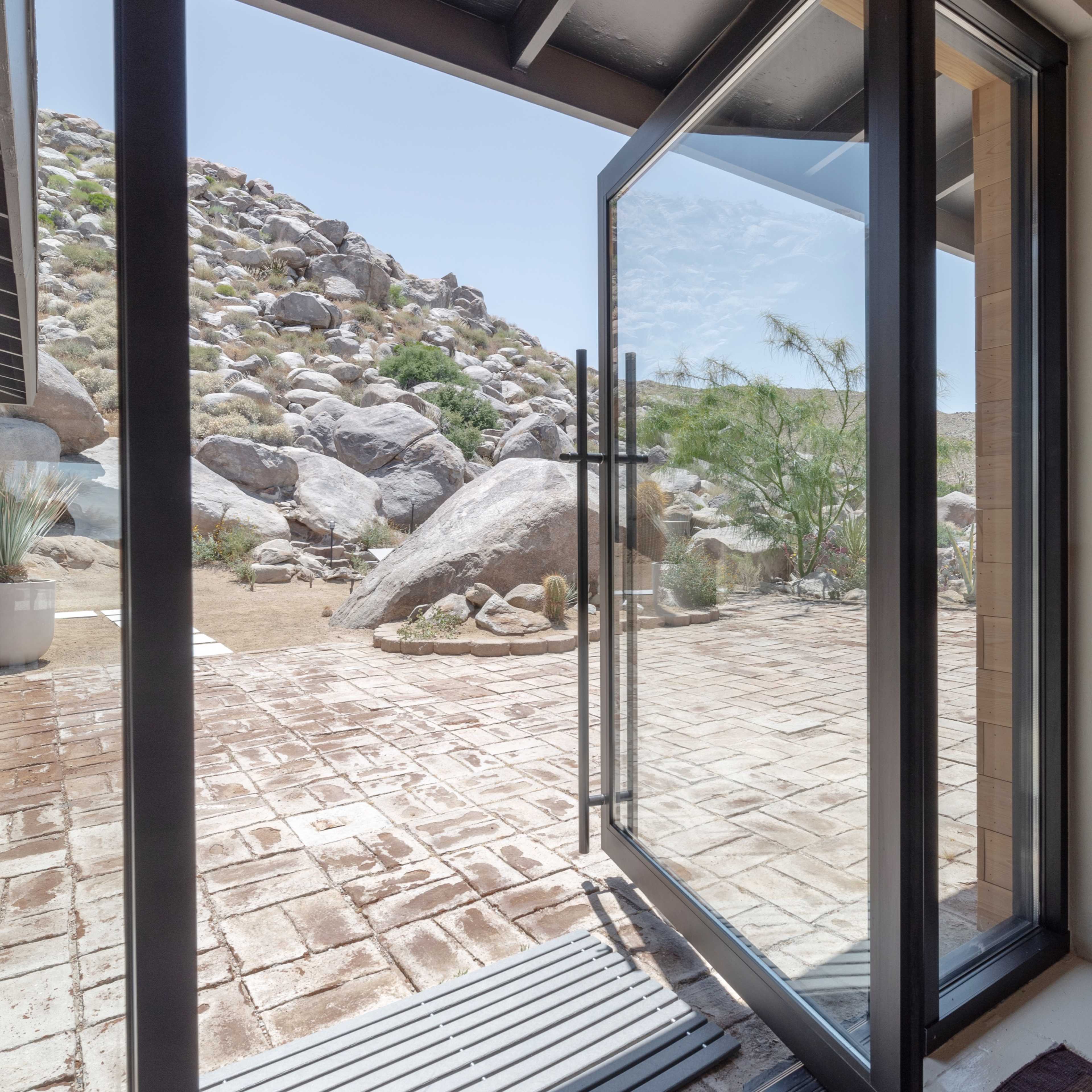An open glass door reveals a patio with large boulders and a rocky hillside in the background.