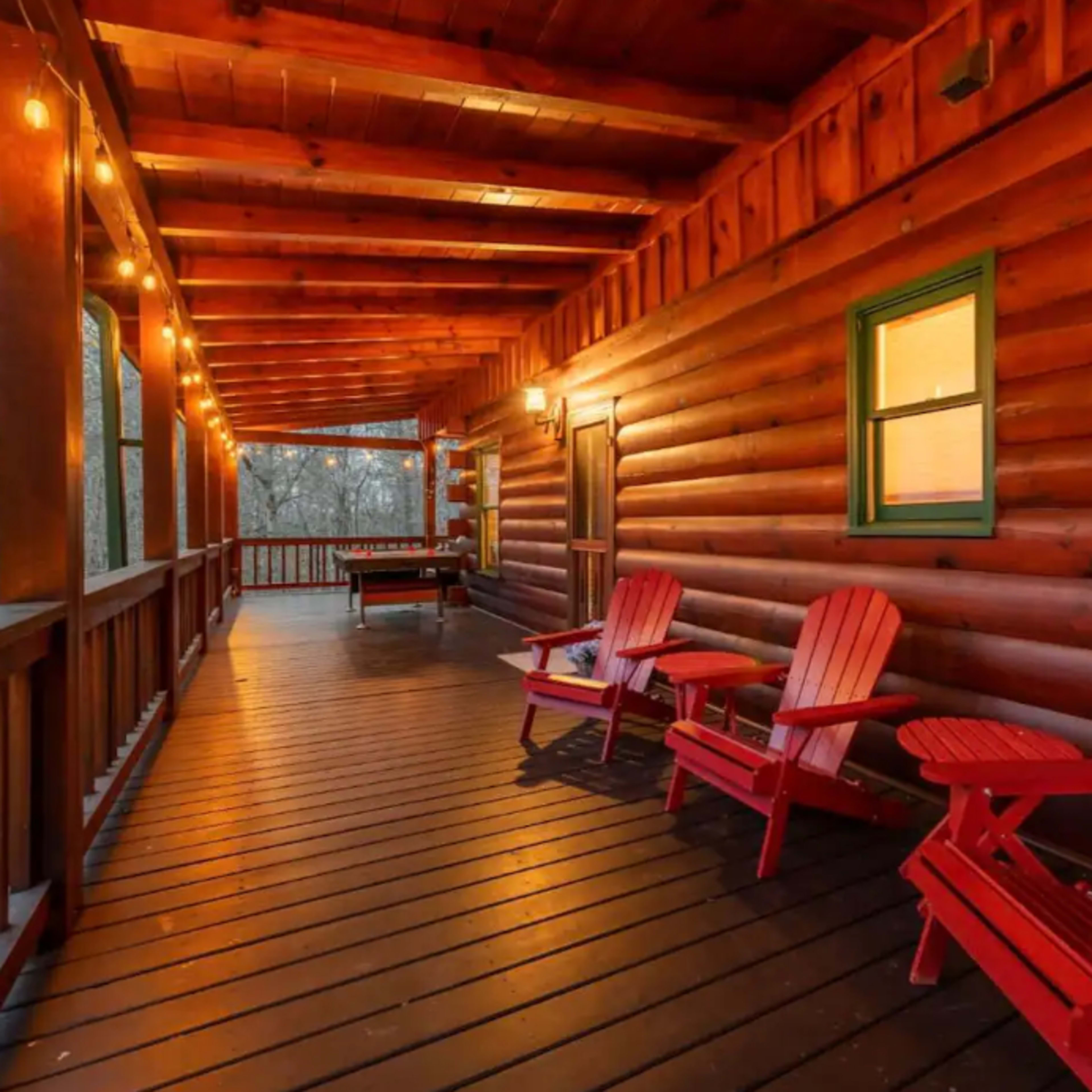 A wooden porch with red Adirondack chairs and warm string lights along the walls of a log cabin.