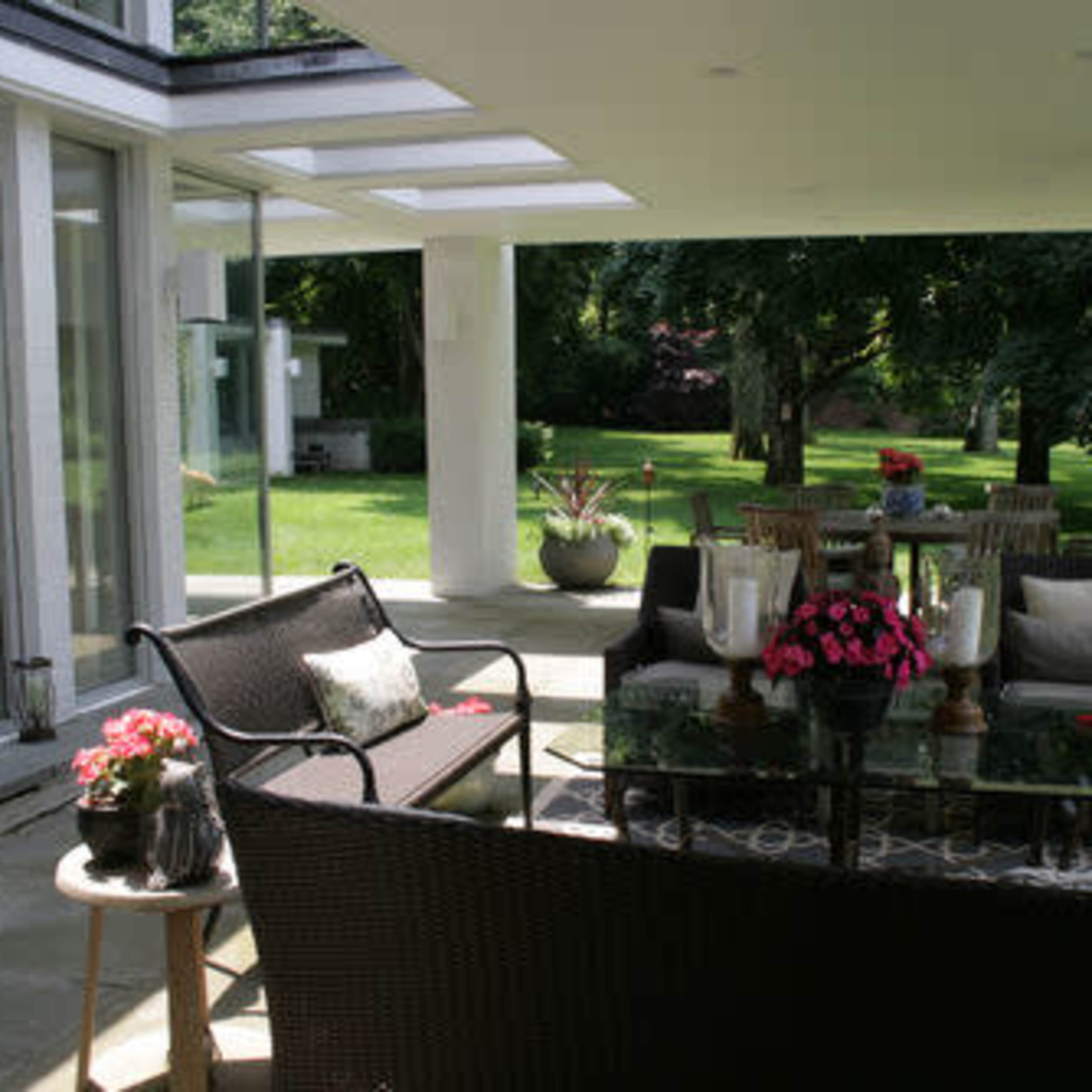 A modern outdoor patio area with seating and a dining table surrounded by greenery.