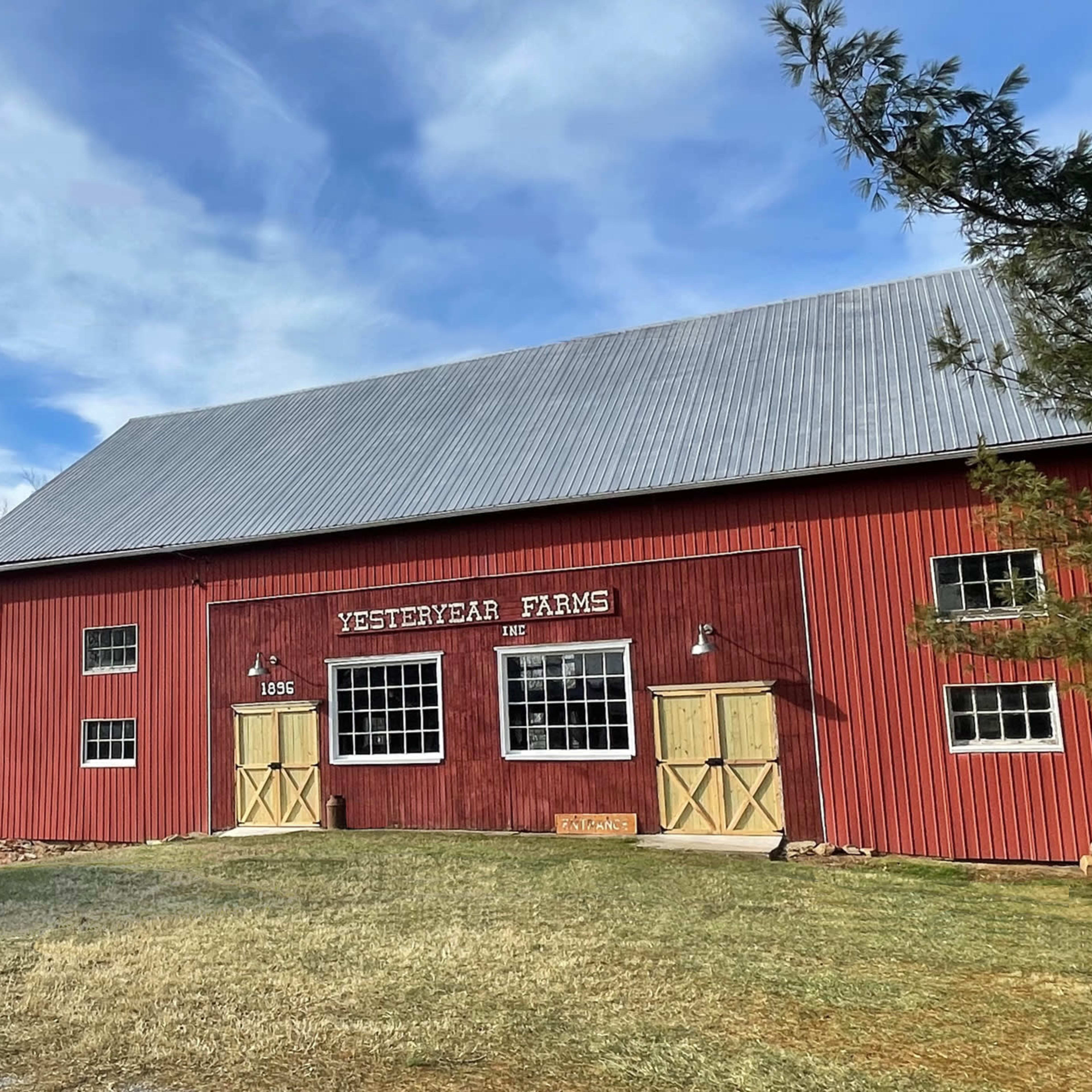 A red barn labeled "Yesteryear Farms" with a gray roof and a gazebo nearby against a backdrop of blue skies.