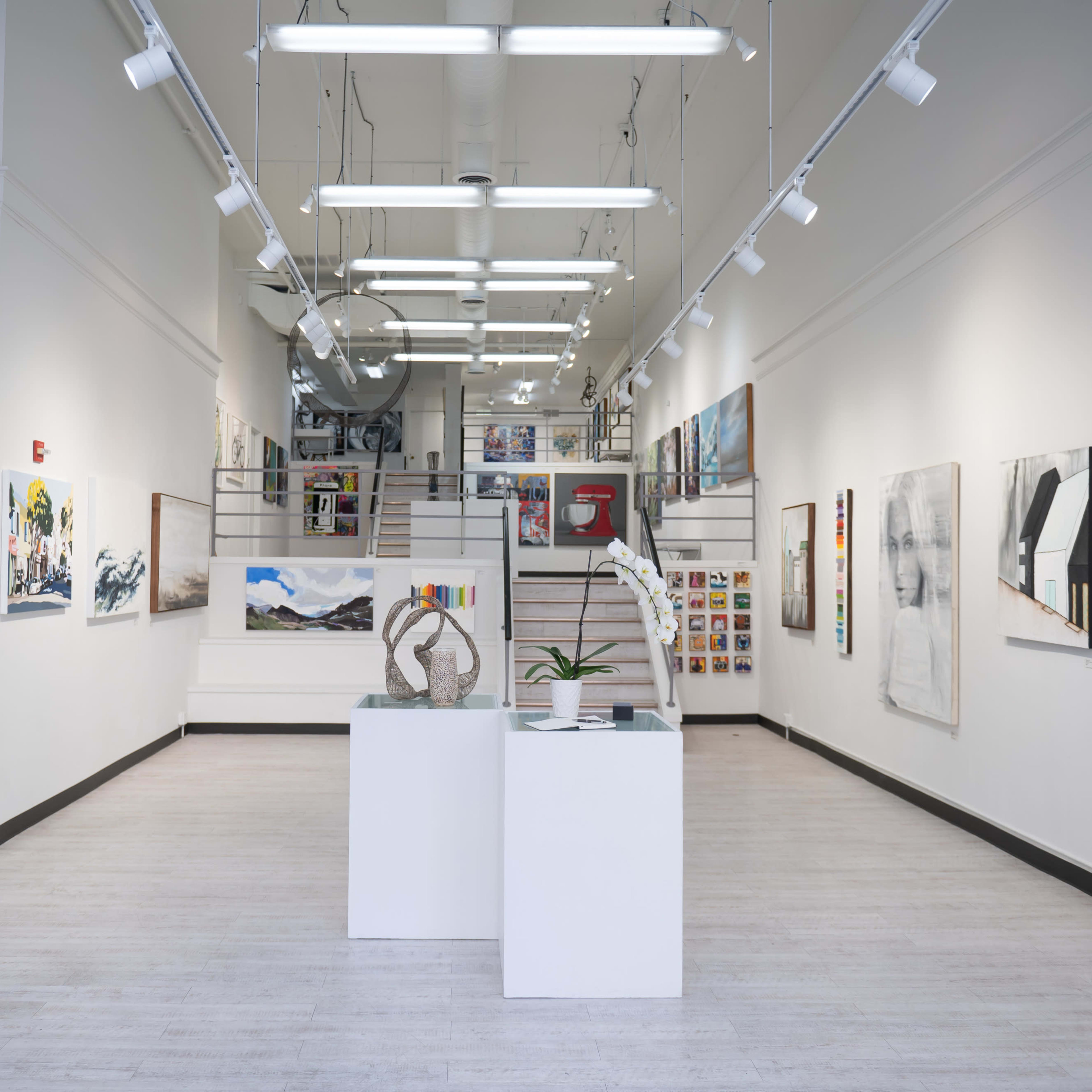 A modern art gallery featuring various paintings and sculptures displayed on the walls and a central pedestal.