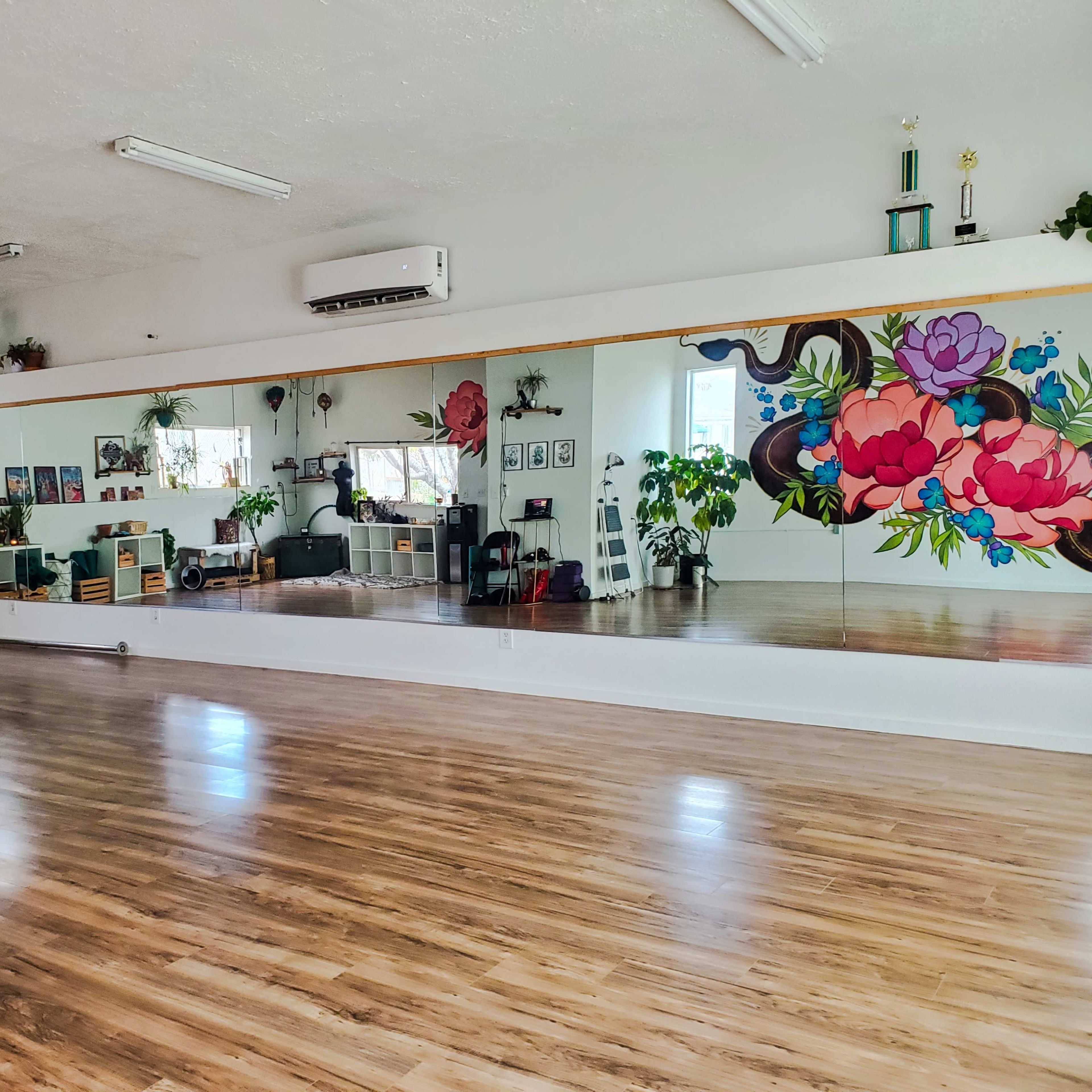 A spacious dance studio with a large mirror, wooden flooring, and colorful wall murals featuring flowers and plants.
