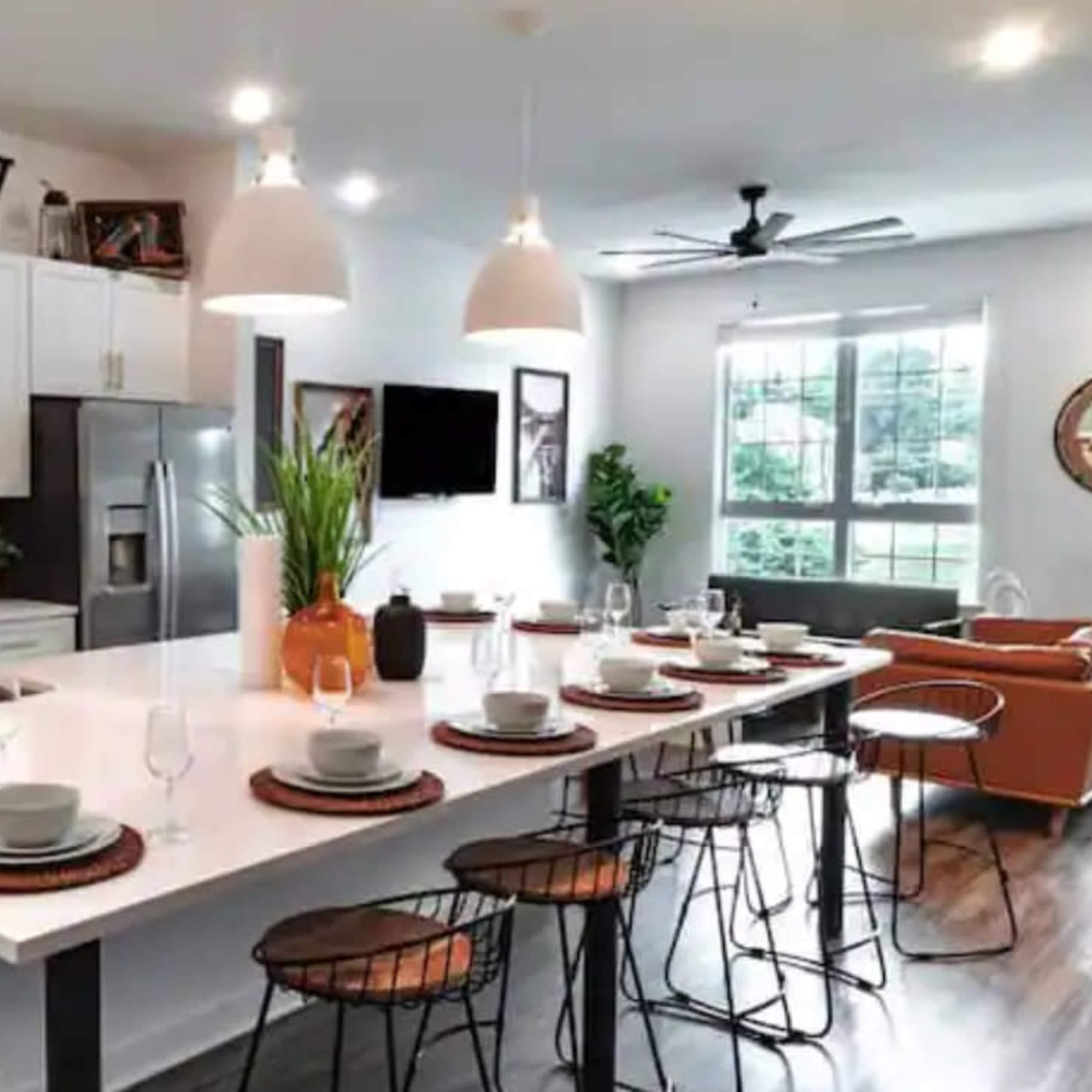 A modern kitchen with a large island featuring dining settings and contemporary appliances, complemented by pendant lighting and a well-lit open space.