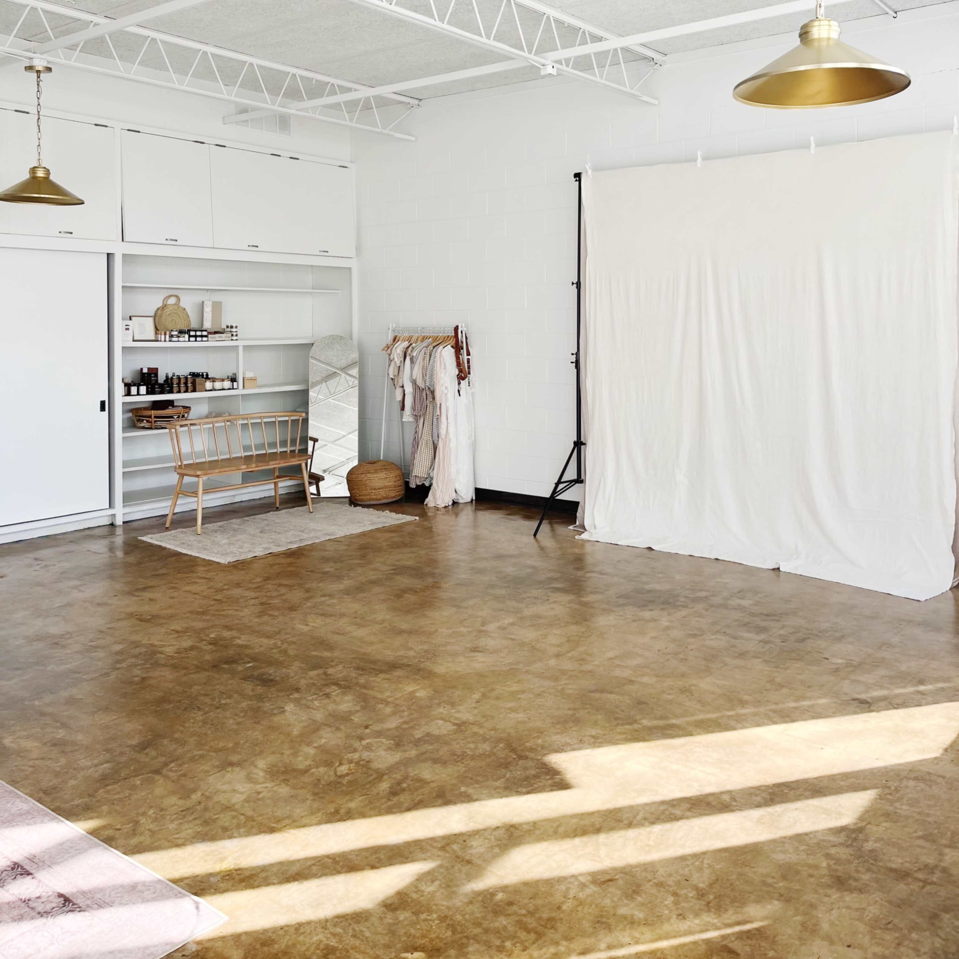 A spacious studio interior with a white backdrop, wooden furniture, and a minimalist clothing rack against a light-colored wall.