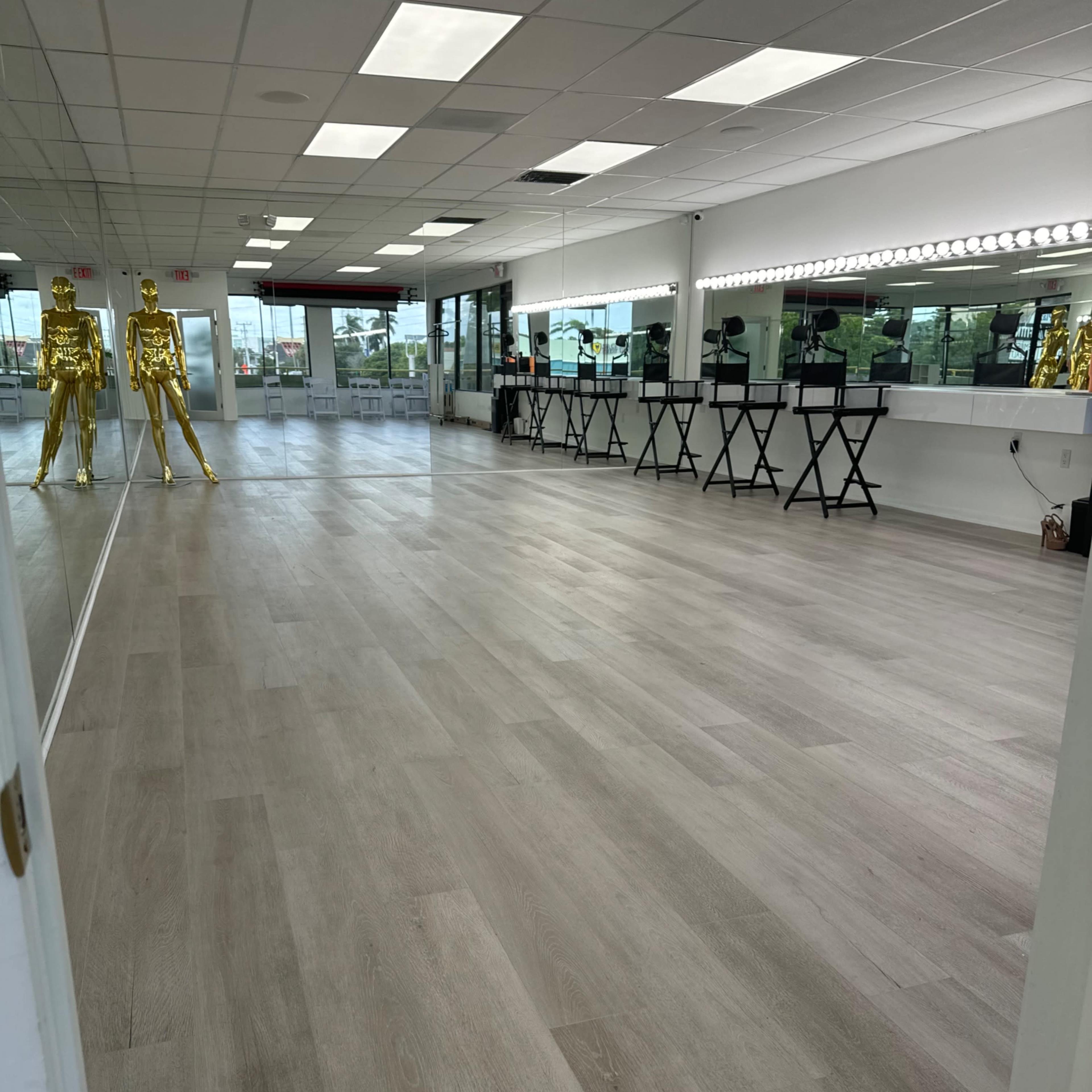 A spacious, well-lit studio with light wooden flooring, two golden mannequins at the front, and a row of black tables along one wall.