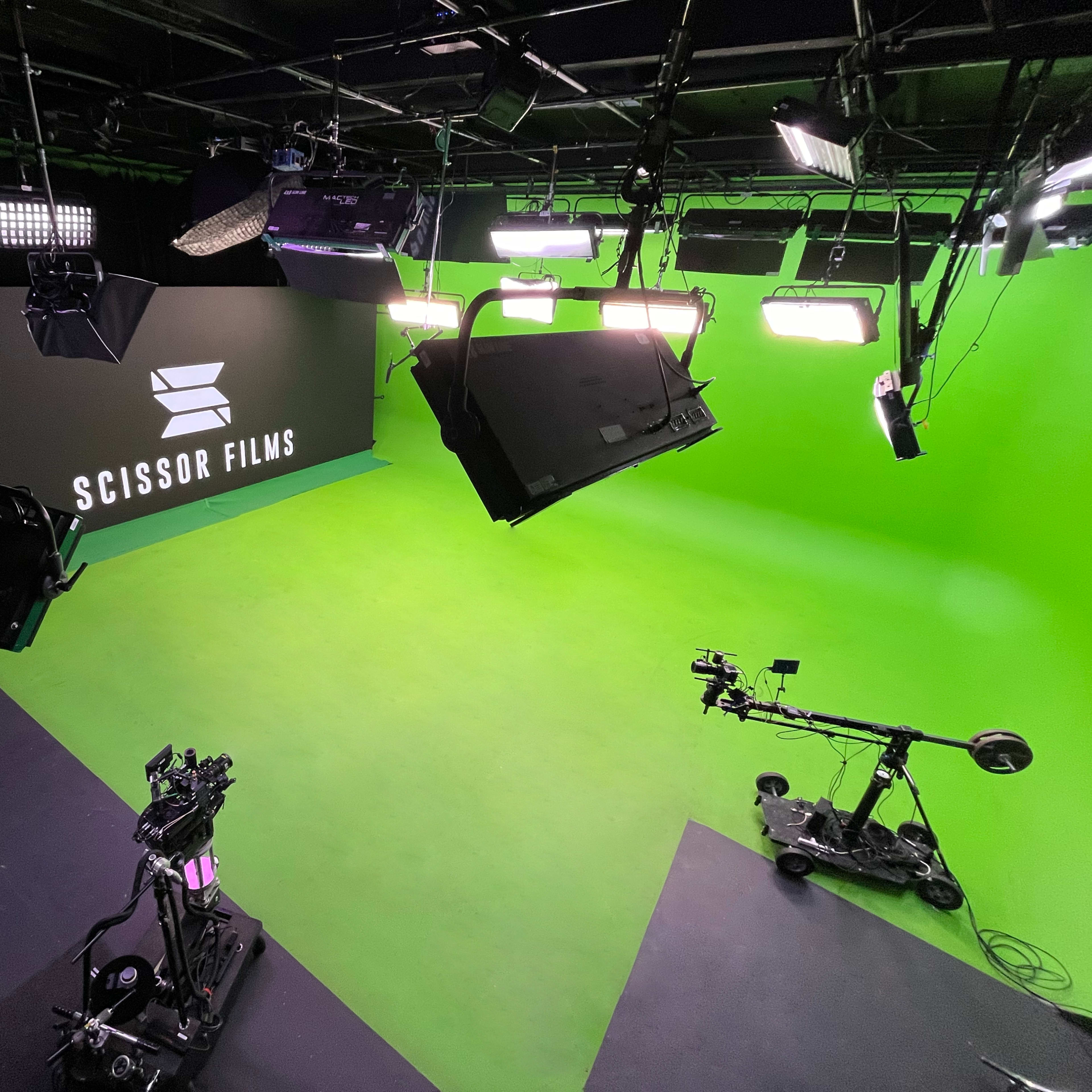 A film studio with a green screen, production equipment, and the logo of "Scissor Films" displayed on the black wall.