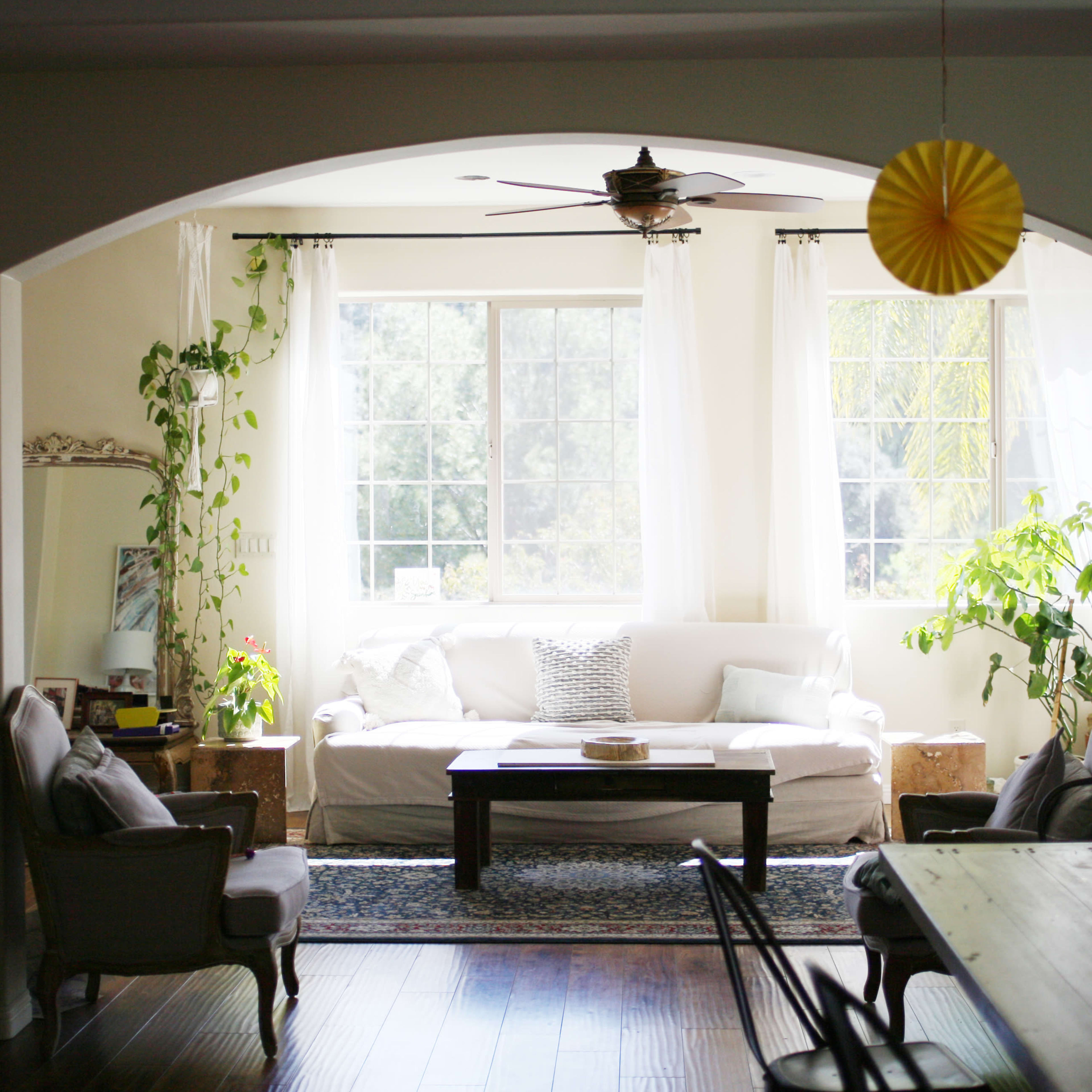 A bright living room with a white sofa, a coffee table, and large windows framed by light curtains.