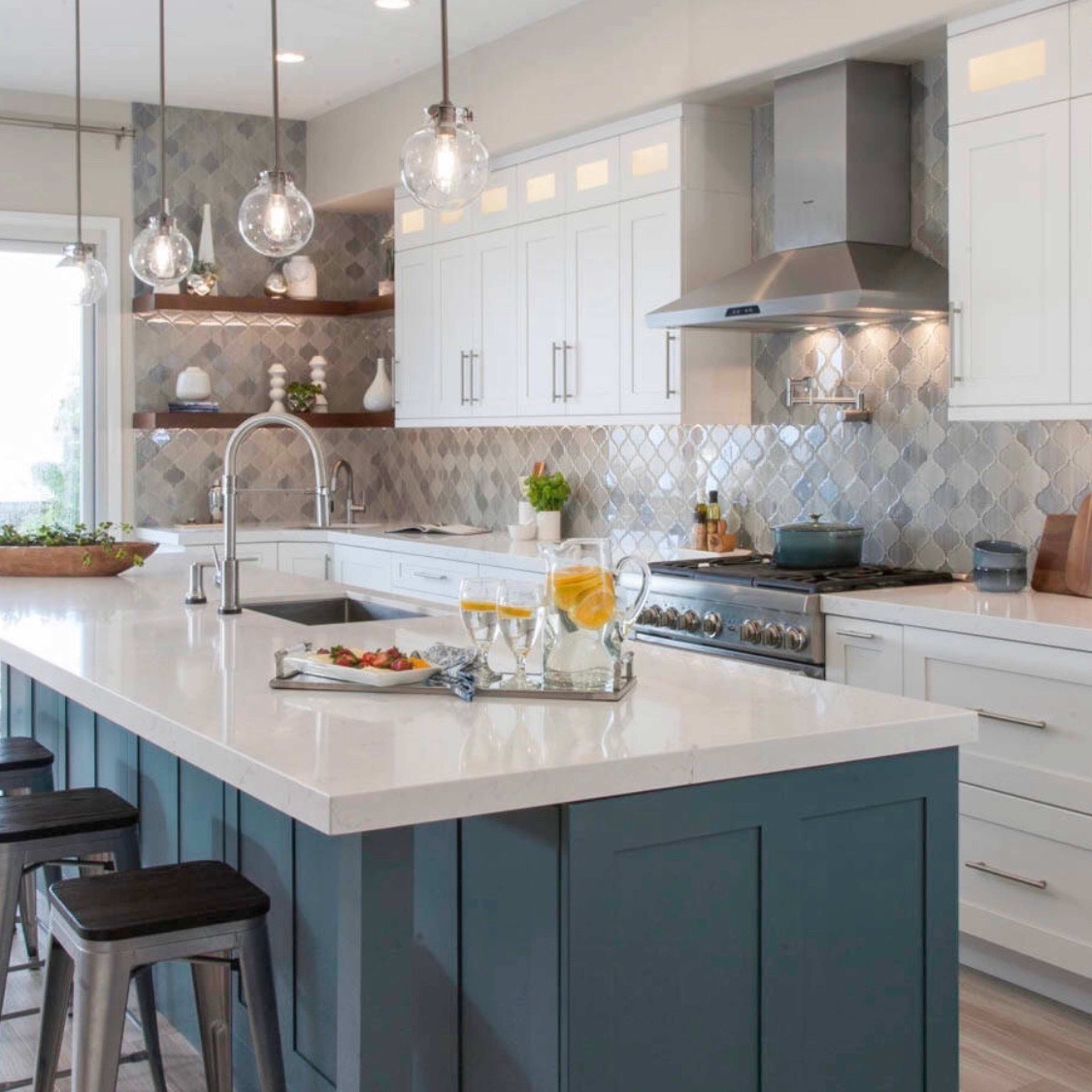A modern kitchen features a large island with a dark blue base, white cabinets, and stainless steel appliances, illuminated by pendant lights.