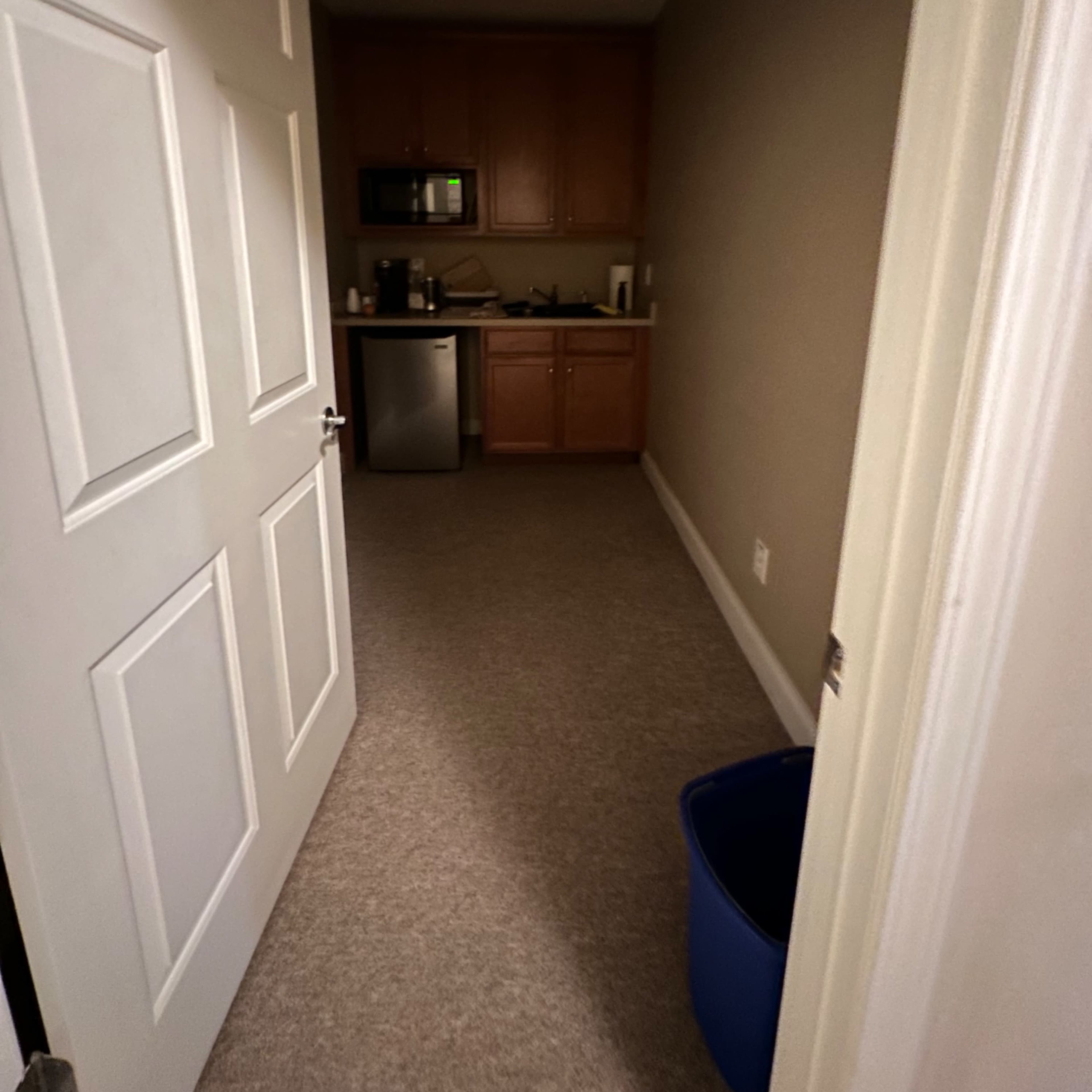 A narrow hallway leading to a small kitchen area with wooden cabinets, a microwave, and a stainless steel refrigerator.