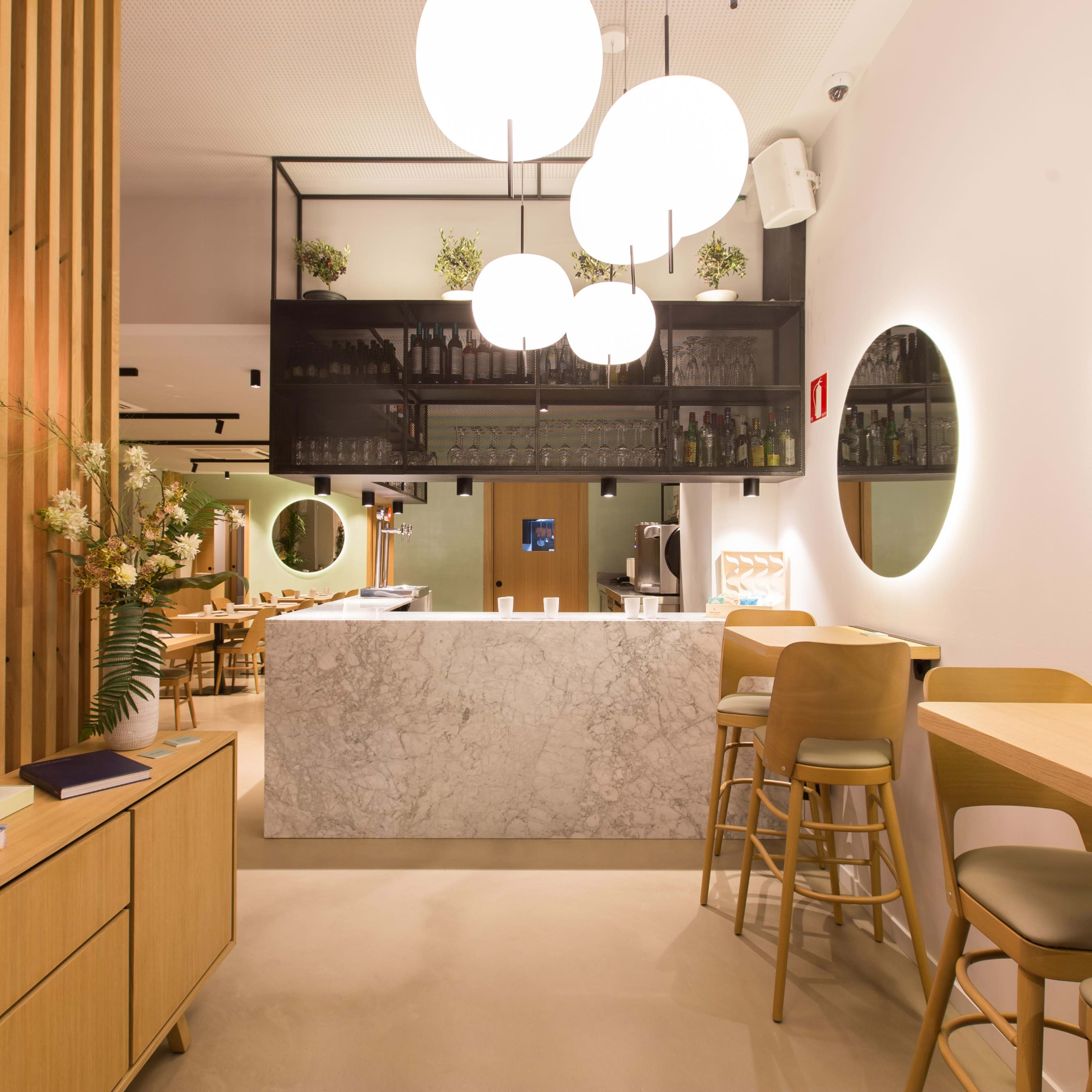 A modern restaurant interior featuring a marble bar, wooden accents, and round mirrors with soft lighting.