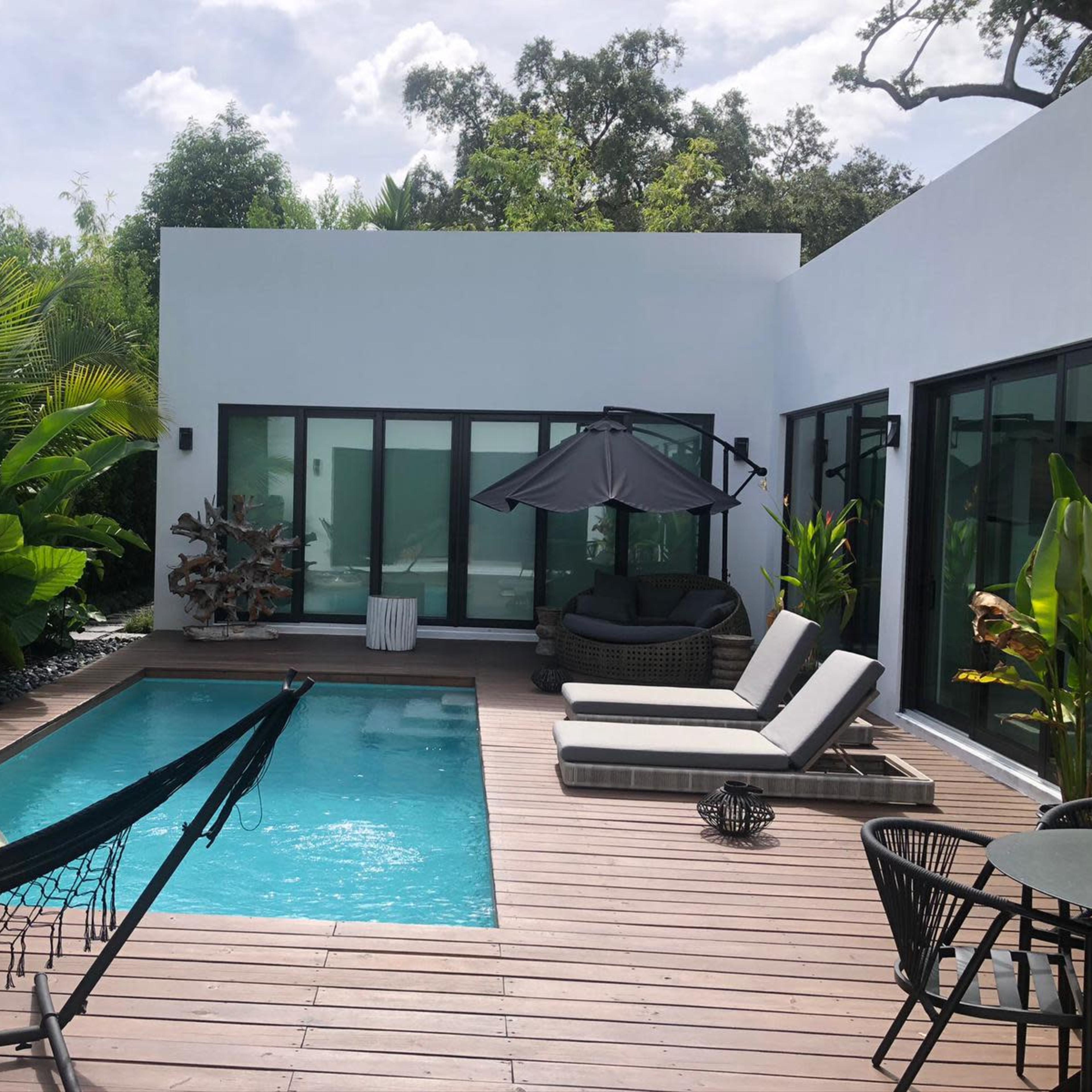 A modern backyard with a swimming pool surrounded by lounge chairs and a hammock, all set amidst lush greenery.