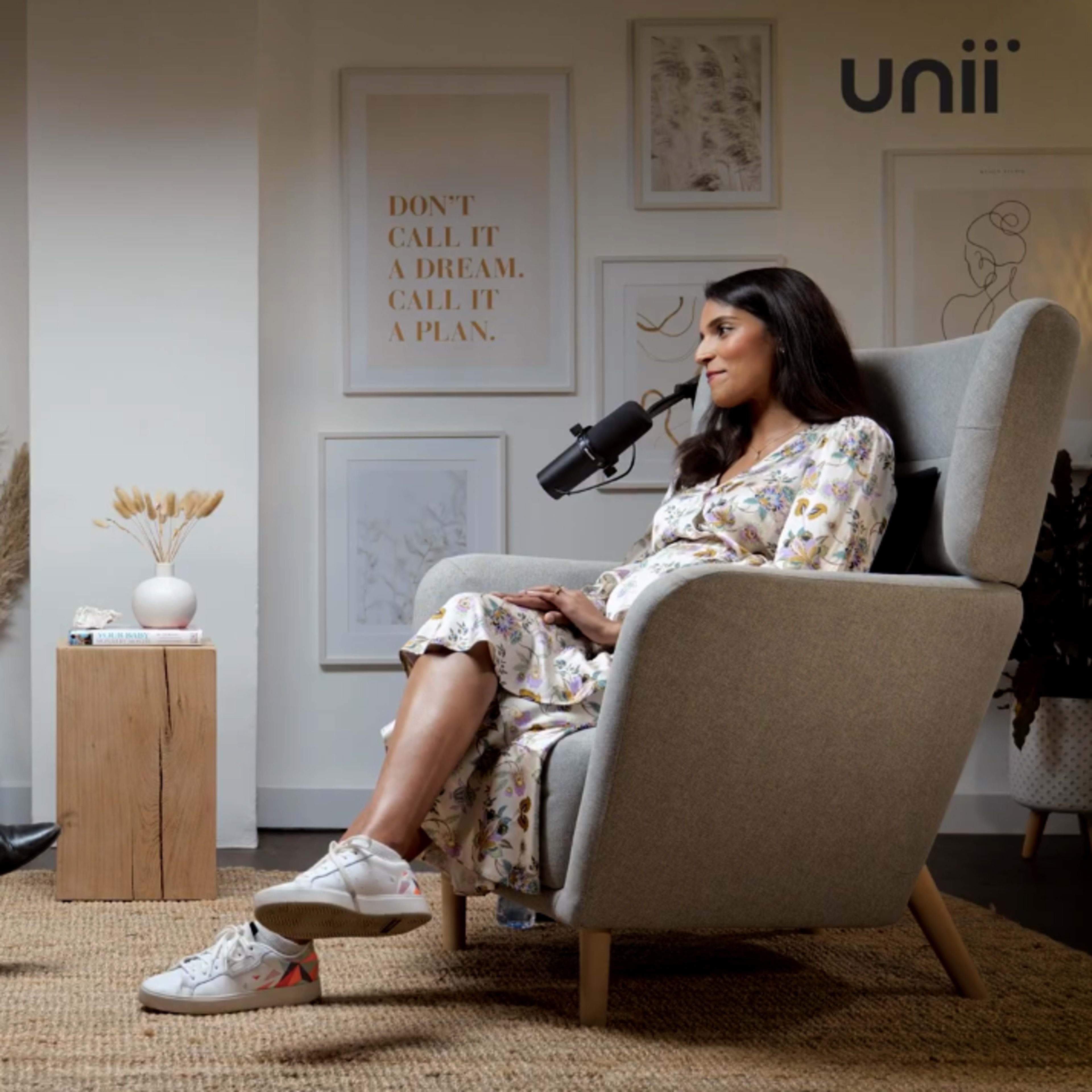 Two women are seated in armchairs facing each other, engaging in conversation, with decorative elements and plants in the background.