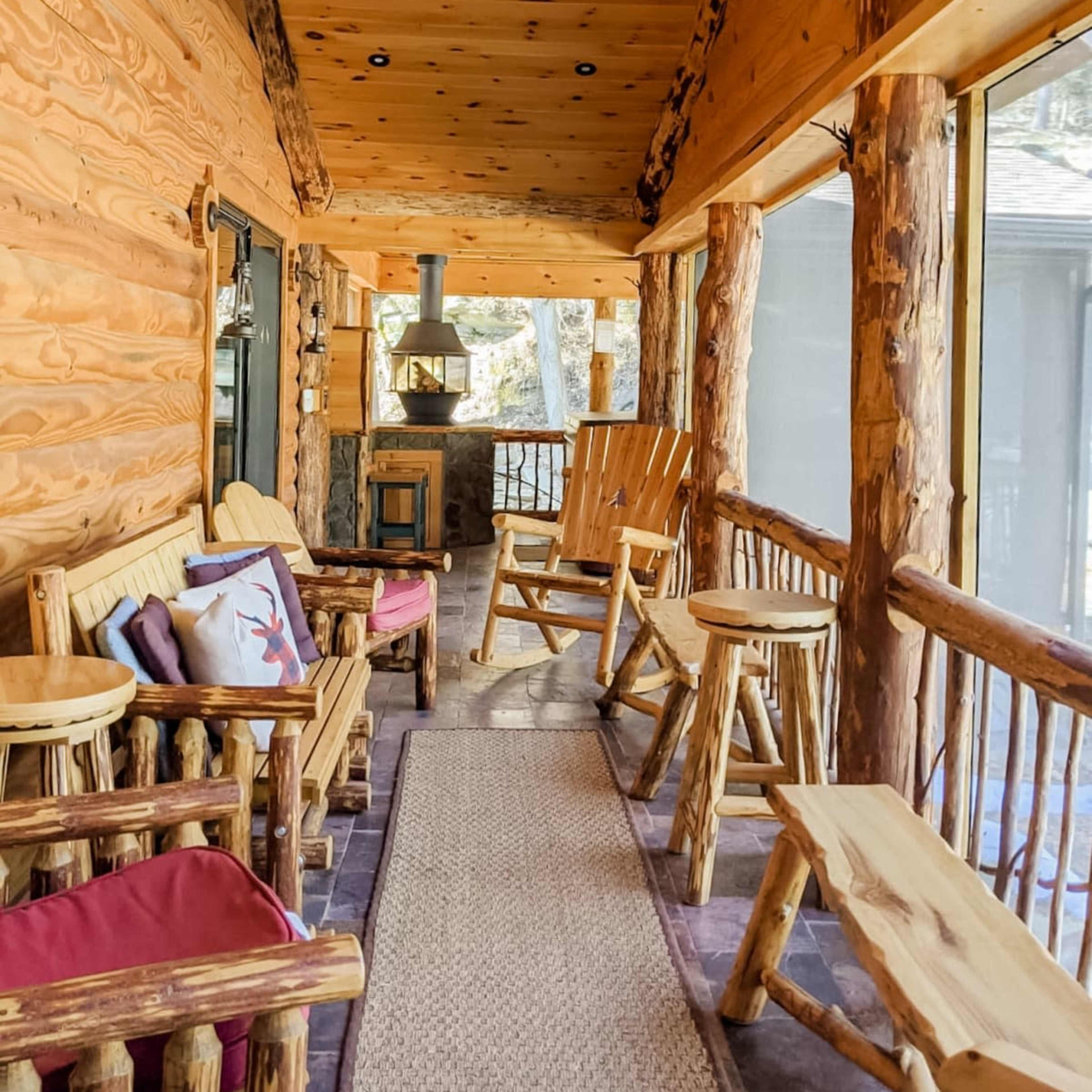 A wooden porch features log furniture, a ceiling fan, and a cozy seating area surrounded by windows.