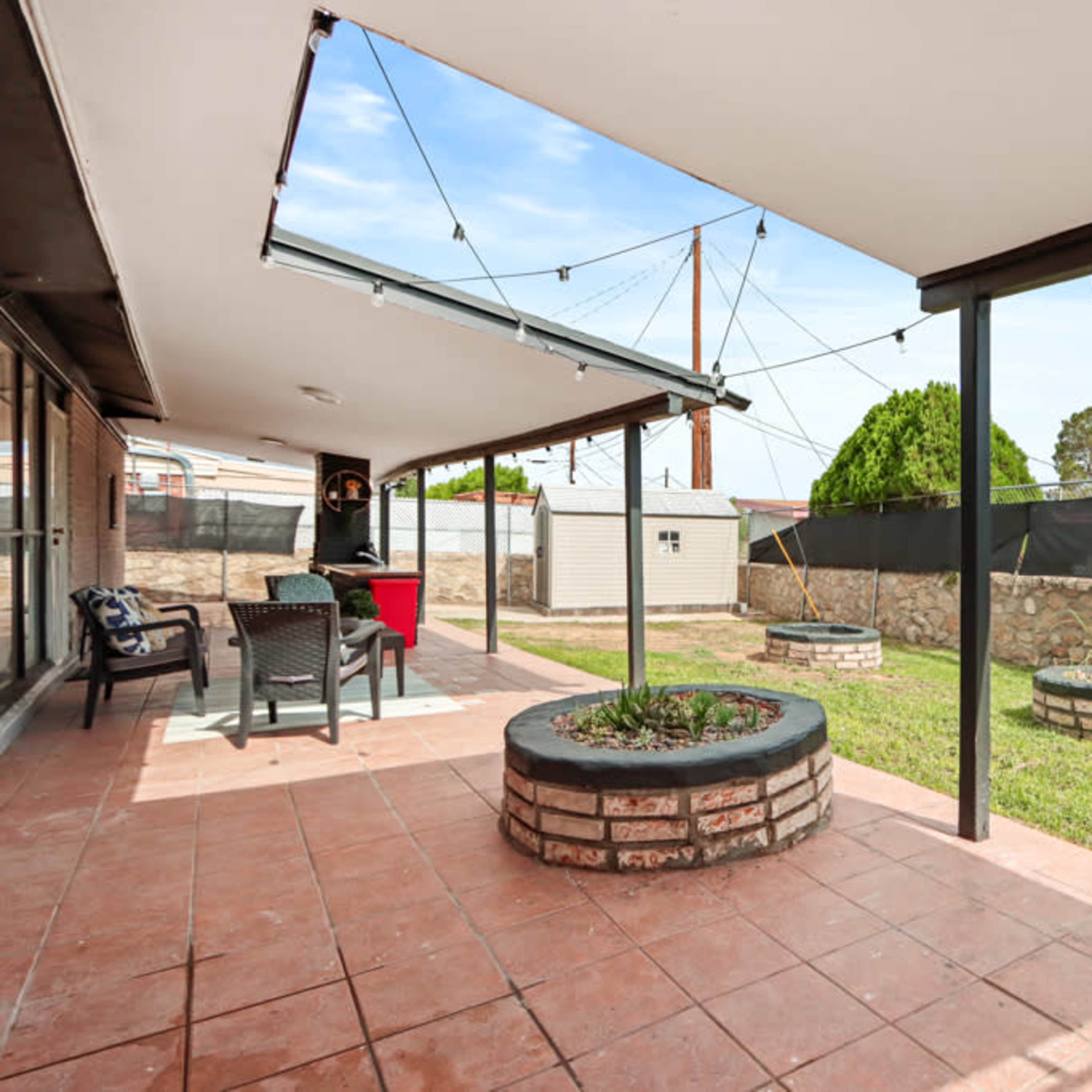 A covered outdoor patio area with stone planters and a grassy space, bordered by a wall.