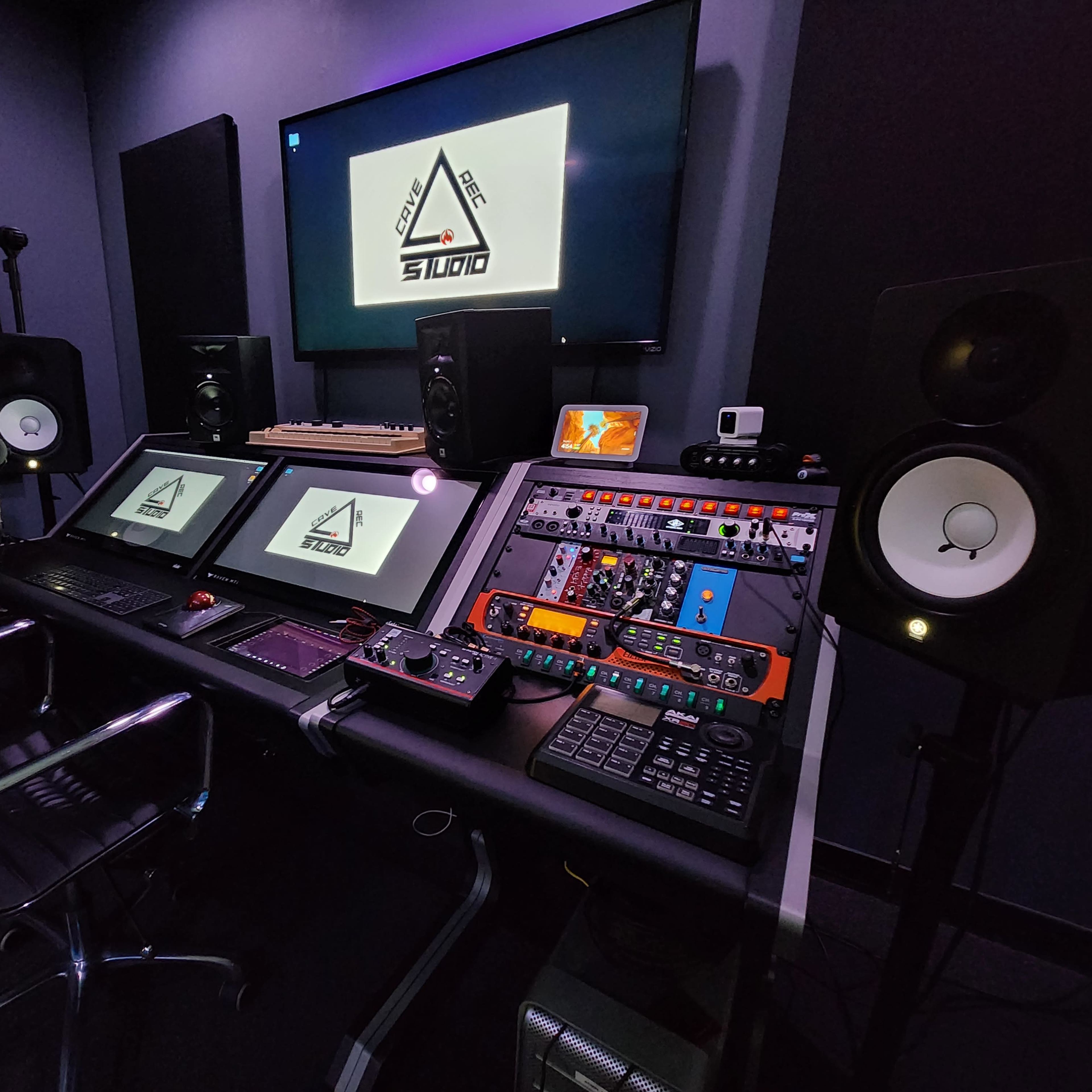 A modern music studio equipped with multiple screens, audio equipment, and speaker monitors.
