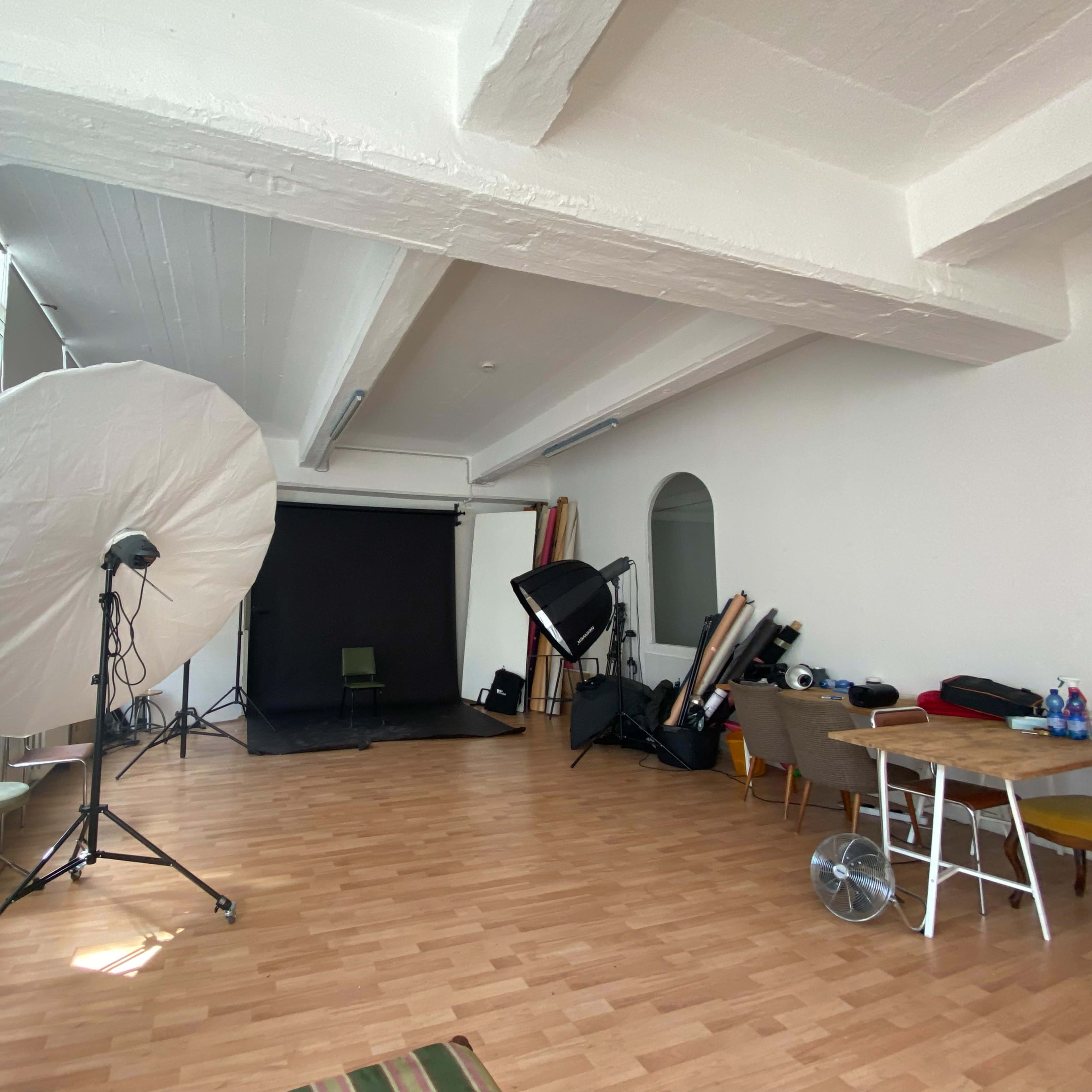 A photography studio with various lighting equipment, a black backdrop, and a wooden floor.