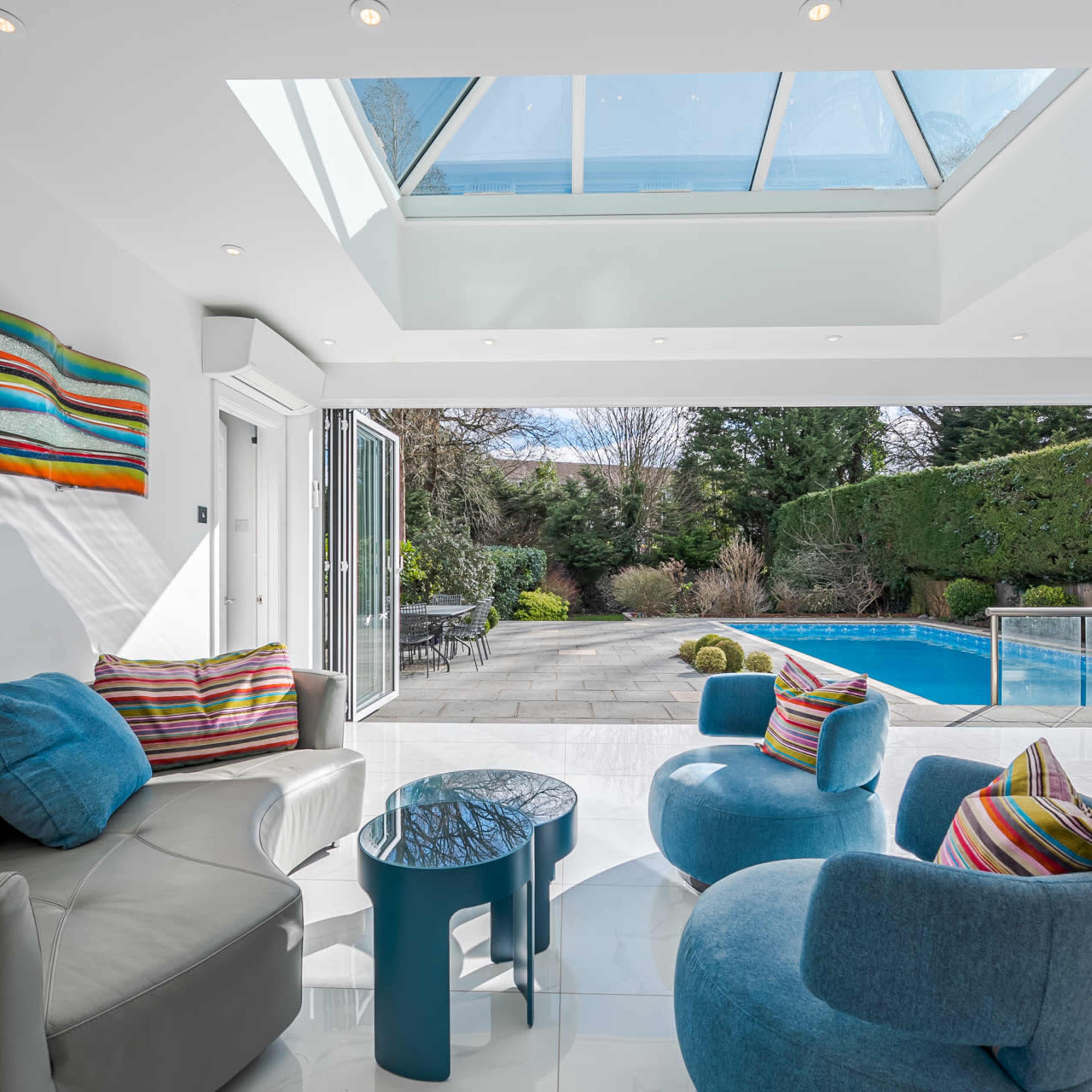 A modern living room features colorful cushions and a view of a pool through large glass doors.