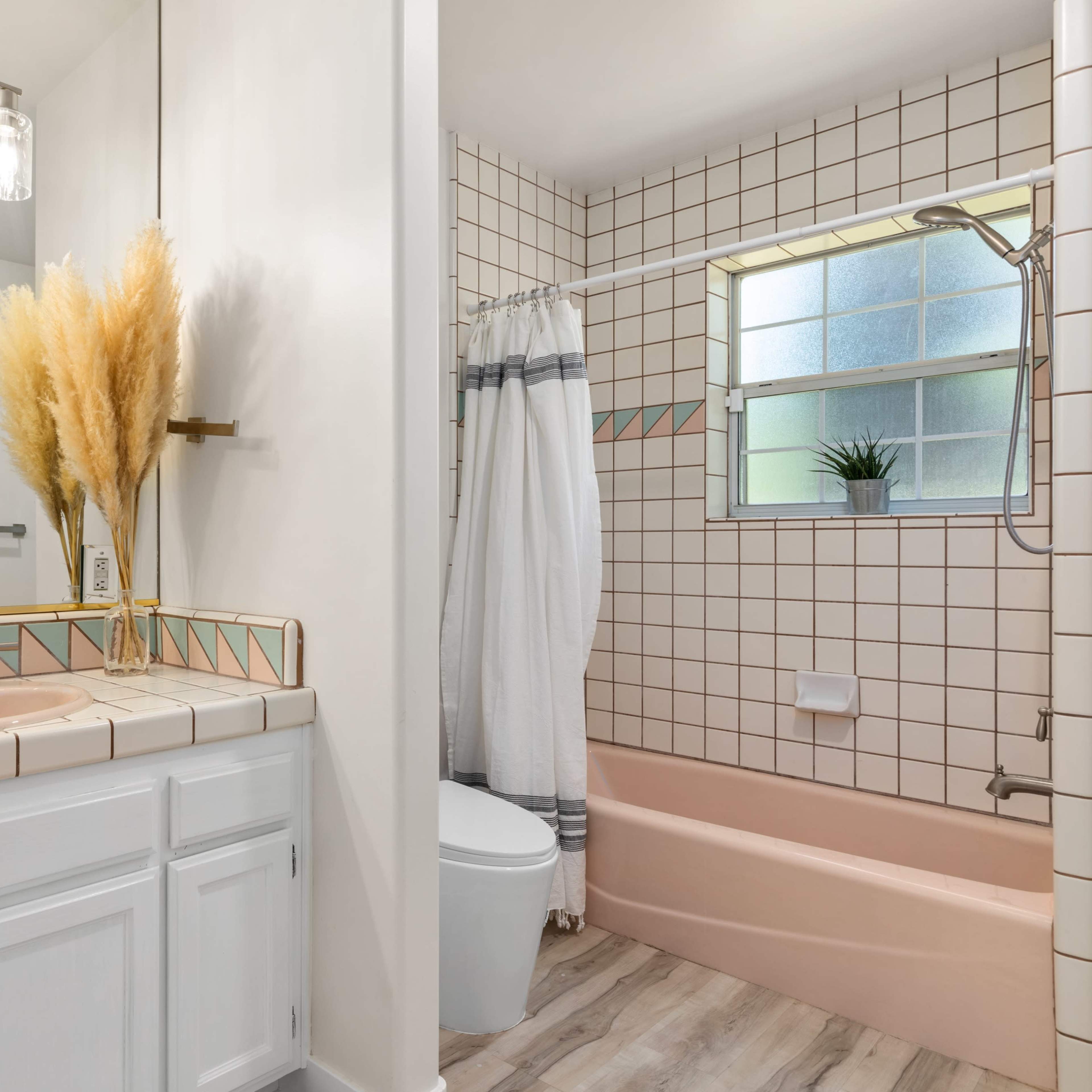 A bathroom features a light-colored tiled counter with a sink, a wall mirror, and a separated shower and bathtub area with pink tiles.
