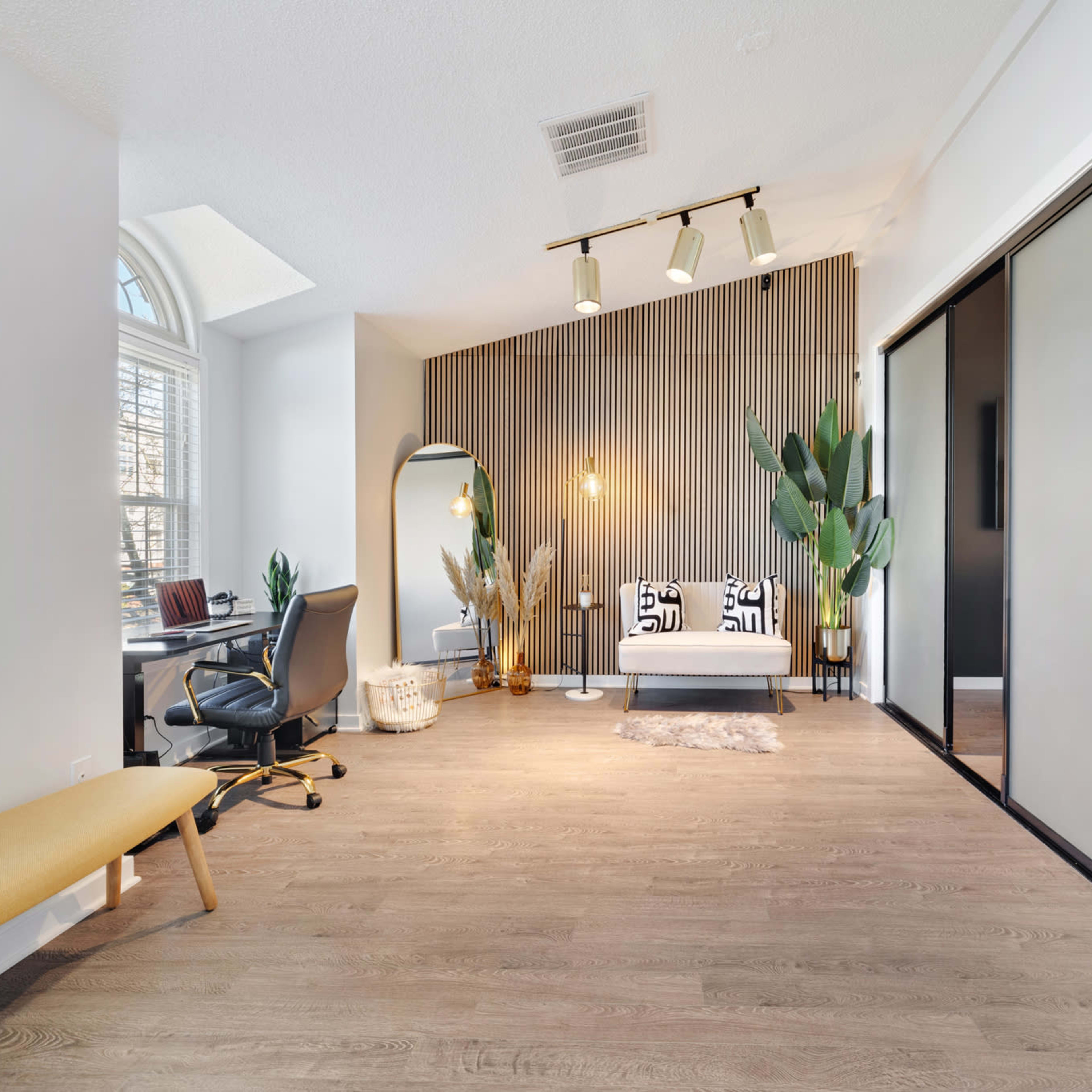 A modern office space featuring a desk with a chair, a decorative wall with plants, and a seating area with a couch, all set on wooden flooring.